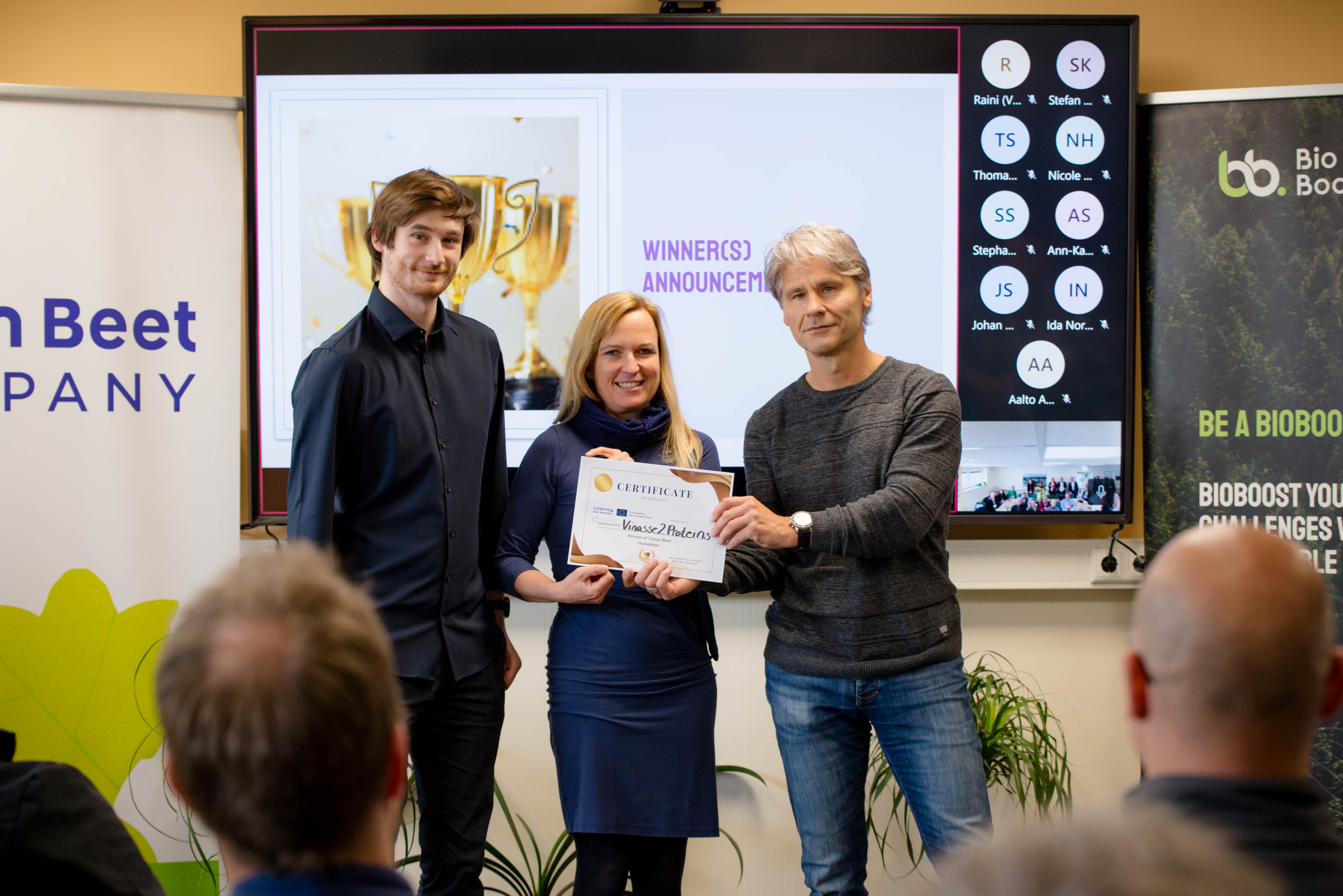 Ein Mann übergibt Urkunde an eine Frau und einen Mann