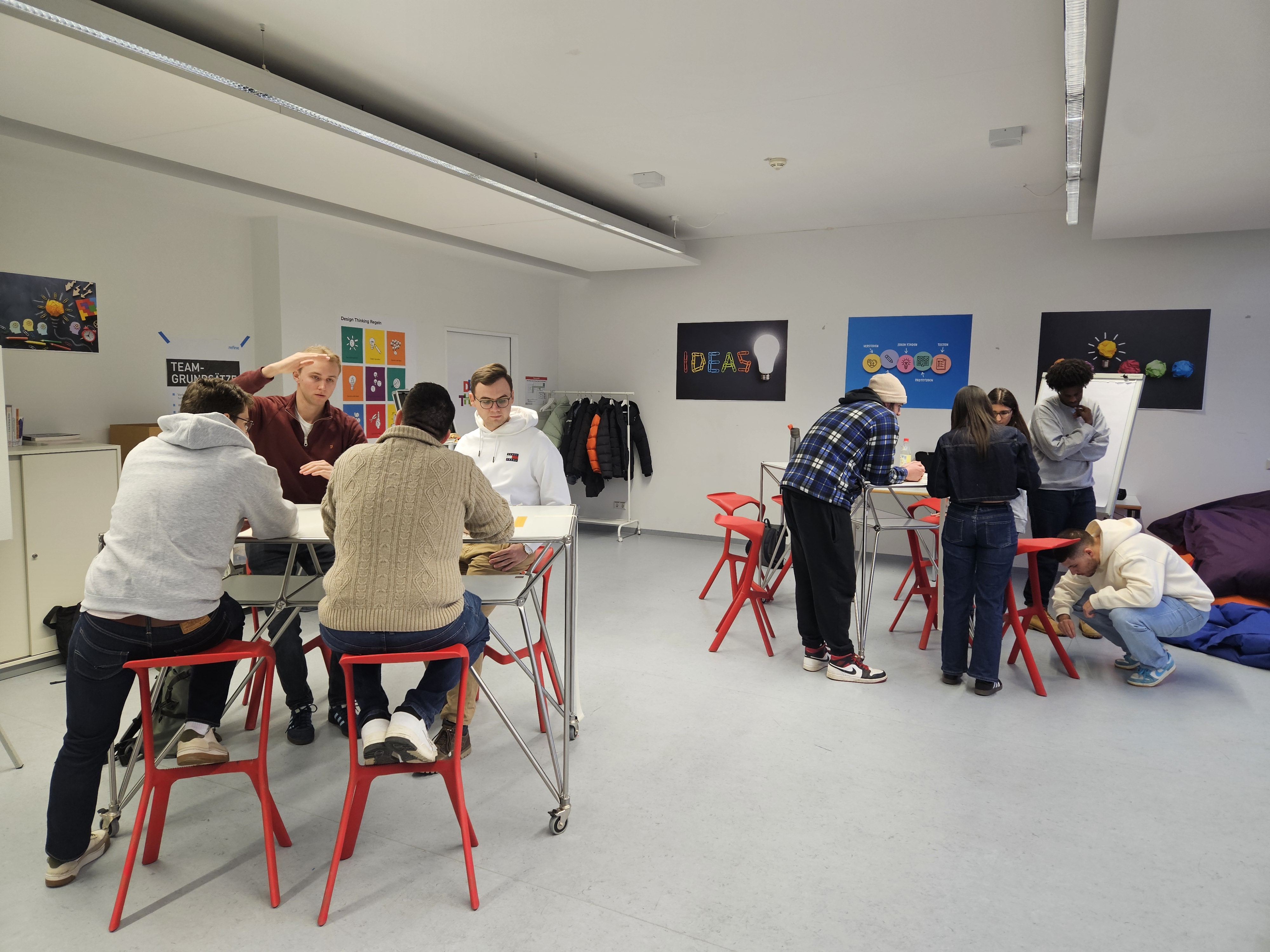 Studierende stehen um Tische herum und bauen Türme aus Spaghetti und Marhsmallow