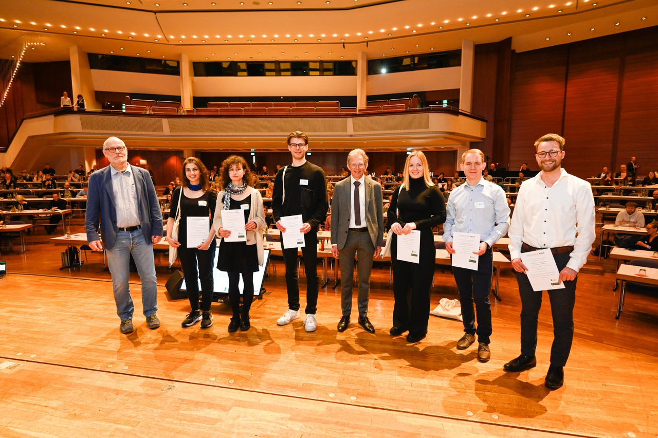 Acht Personen auf Bühne bei Urkundenverleihung