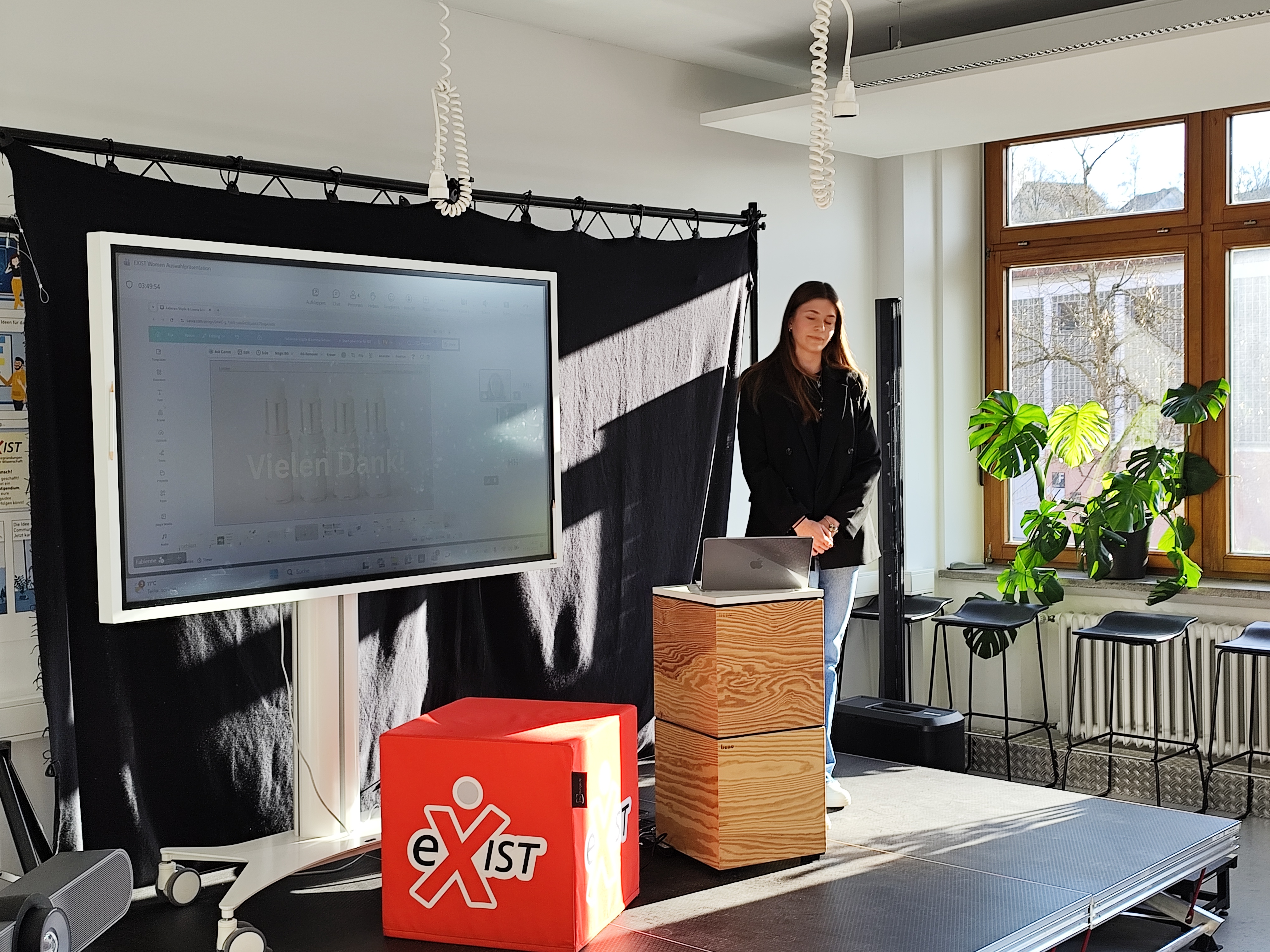 Frau steht auf einer kleinen Bühne und präsentiert ihre Gründungsidee