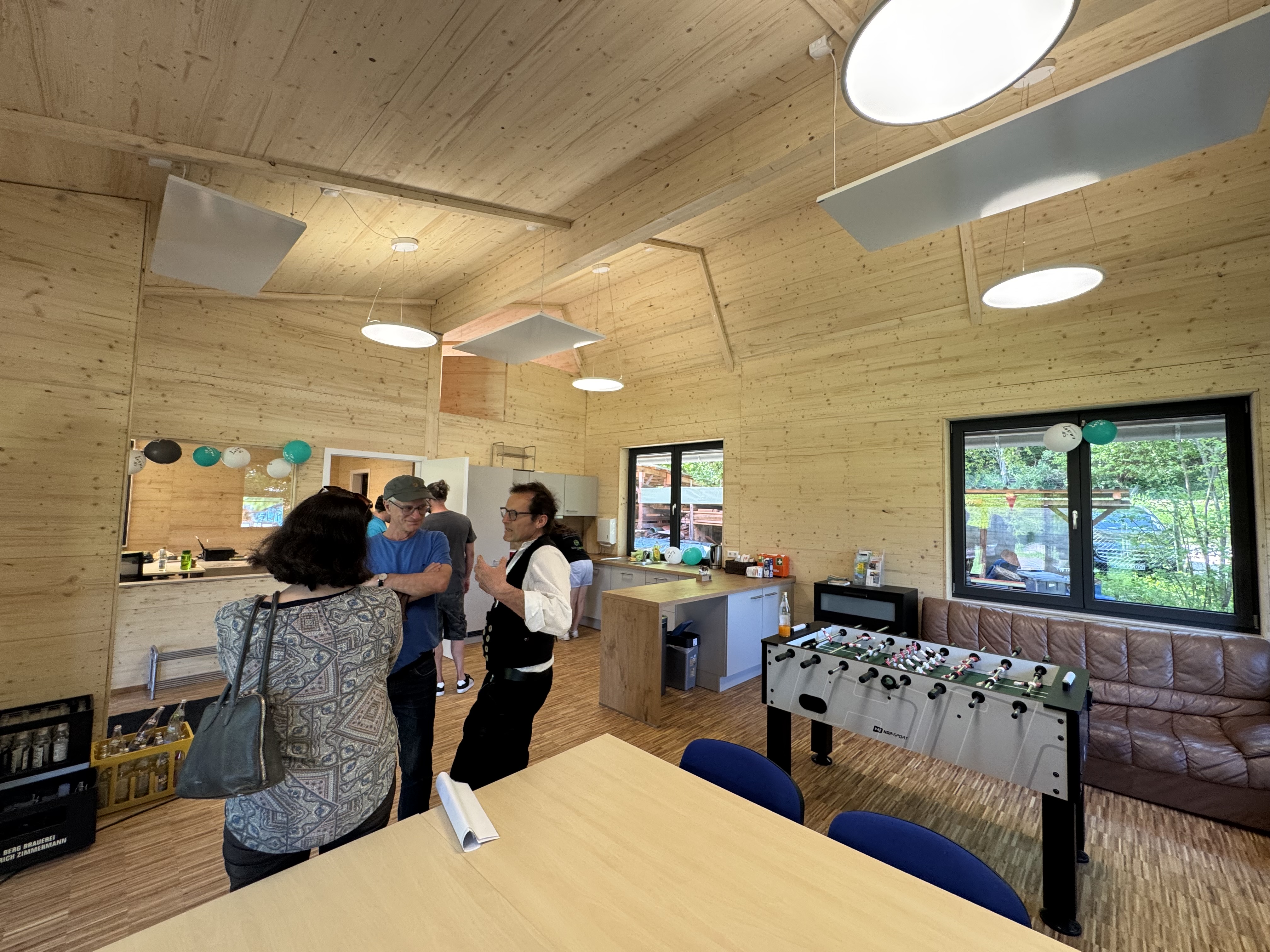 Personen stehen in einem Holzgebäude und unterhalten sich