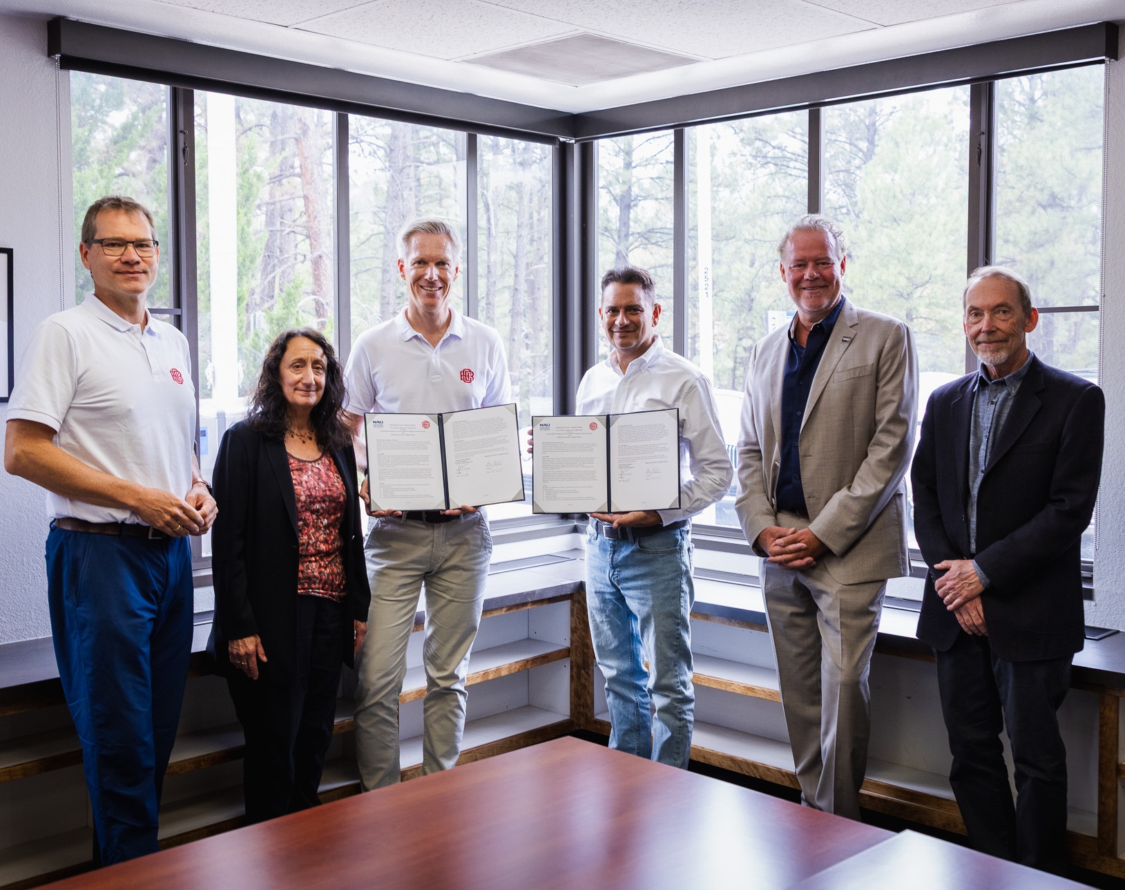 Sechs Personen stehen in einem Raum. Zwei präsentieren unterschriebene Verträge