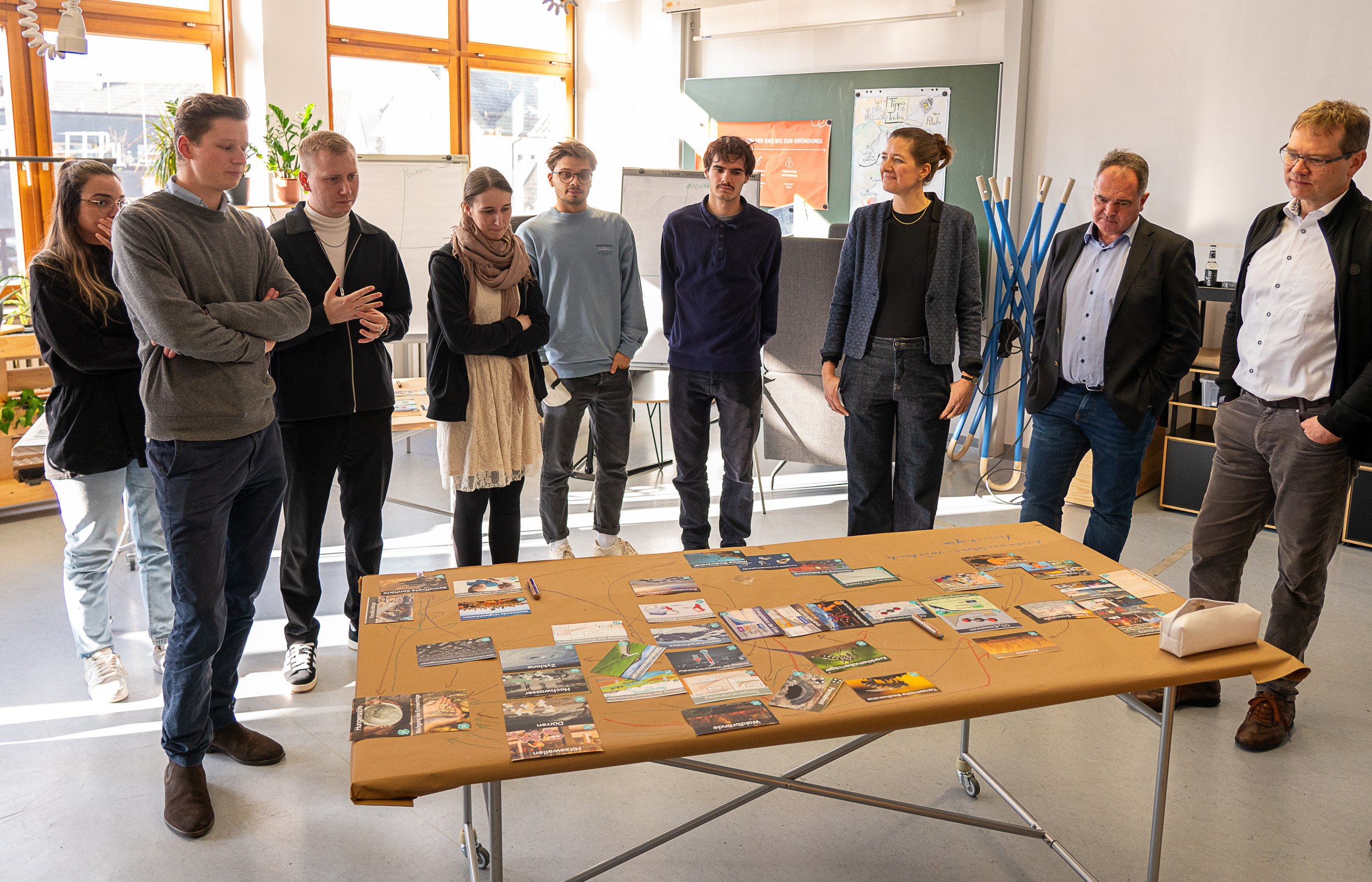 Personen stehen um einen Tisch mit verschiedenen Karten