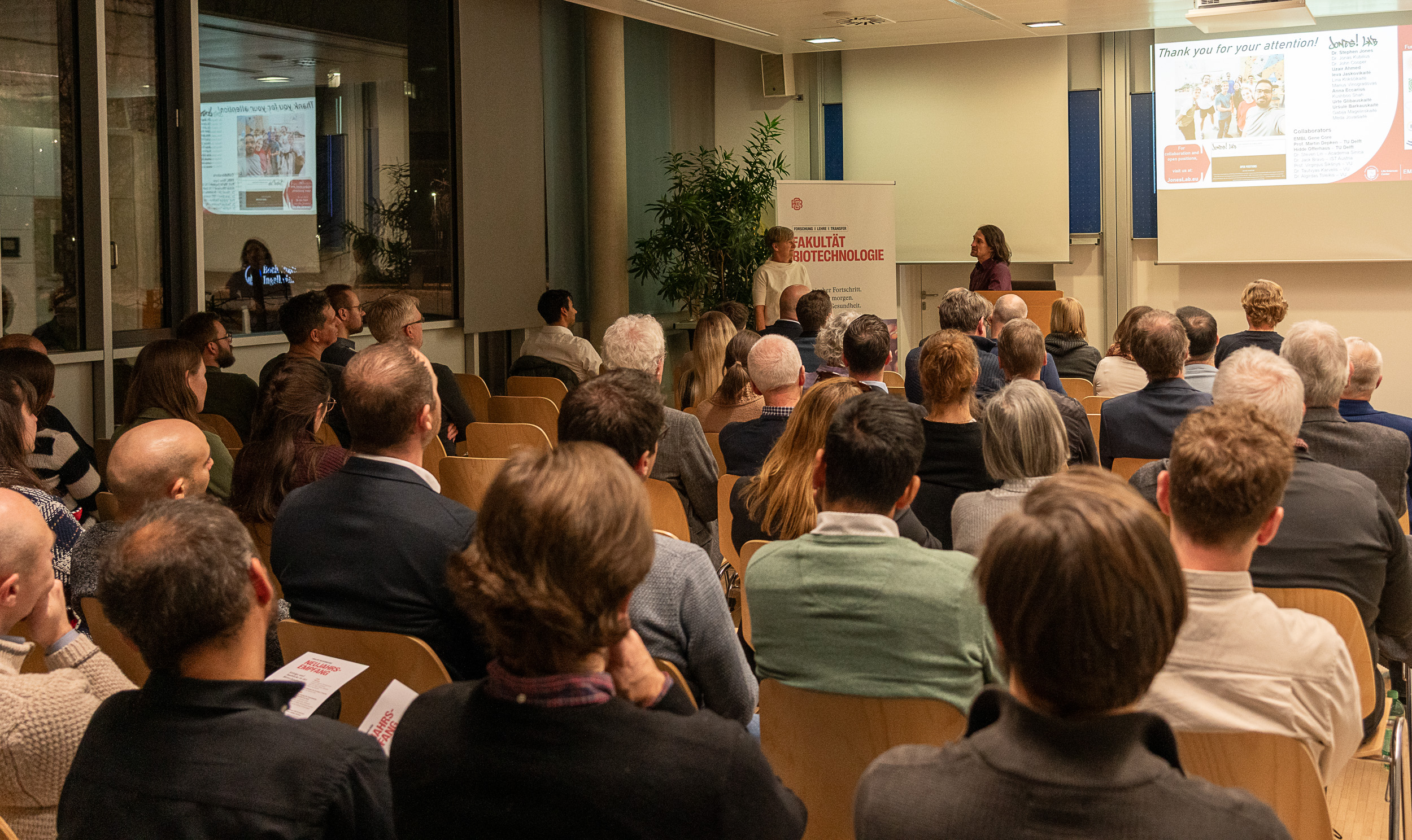 Personen sitzen aufgereiht in einem Raum bei einem Vortrag 