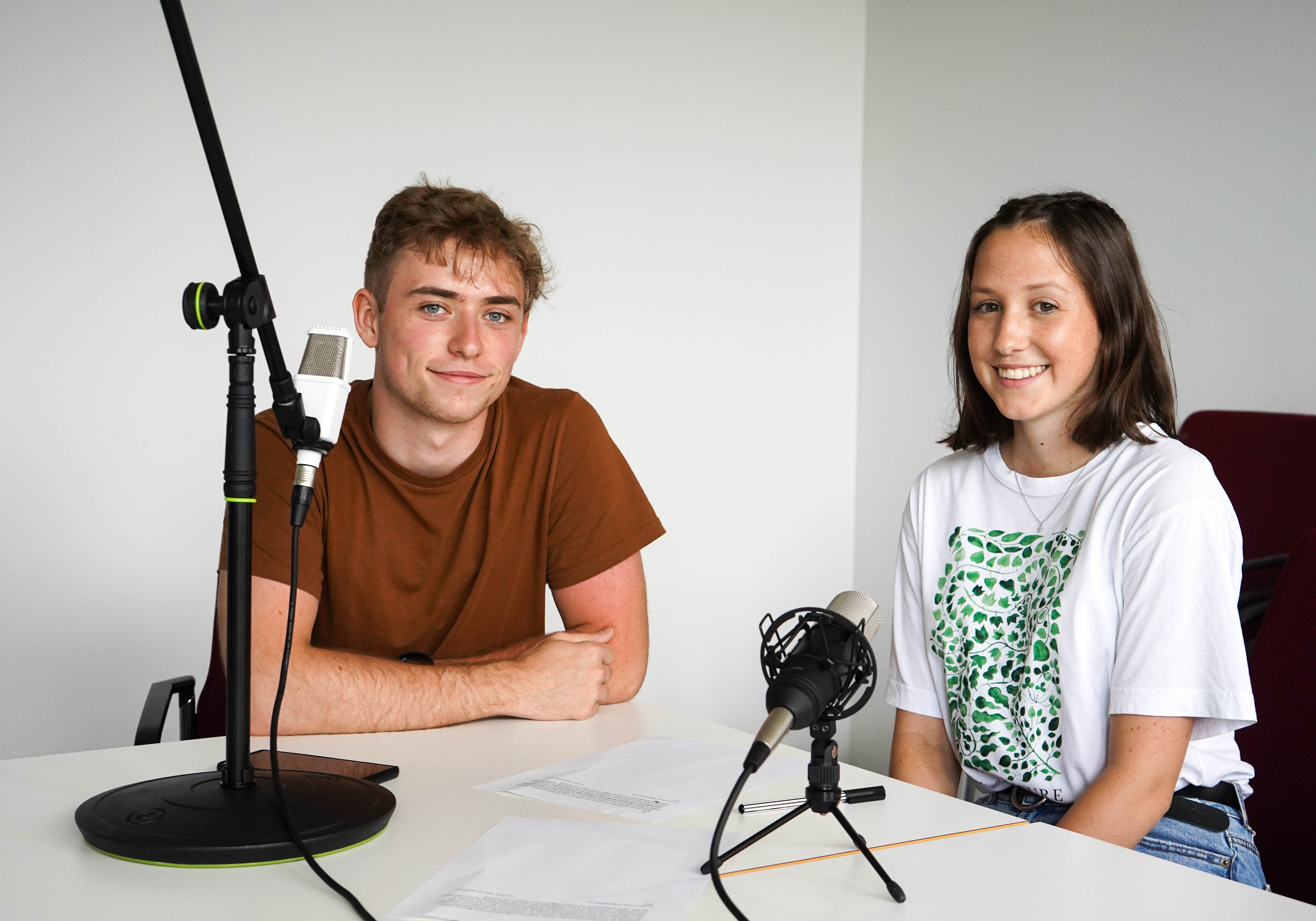 Eine Frau und ein Mann an einem Tisch mit Podcastmikrofonen. 