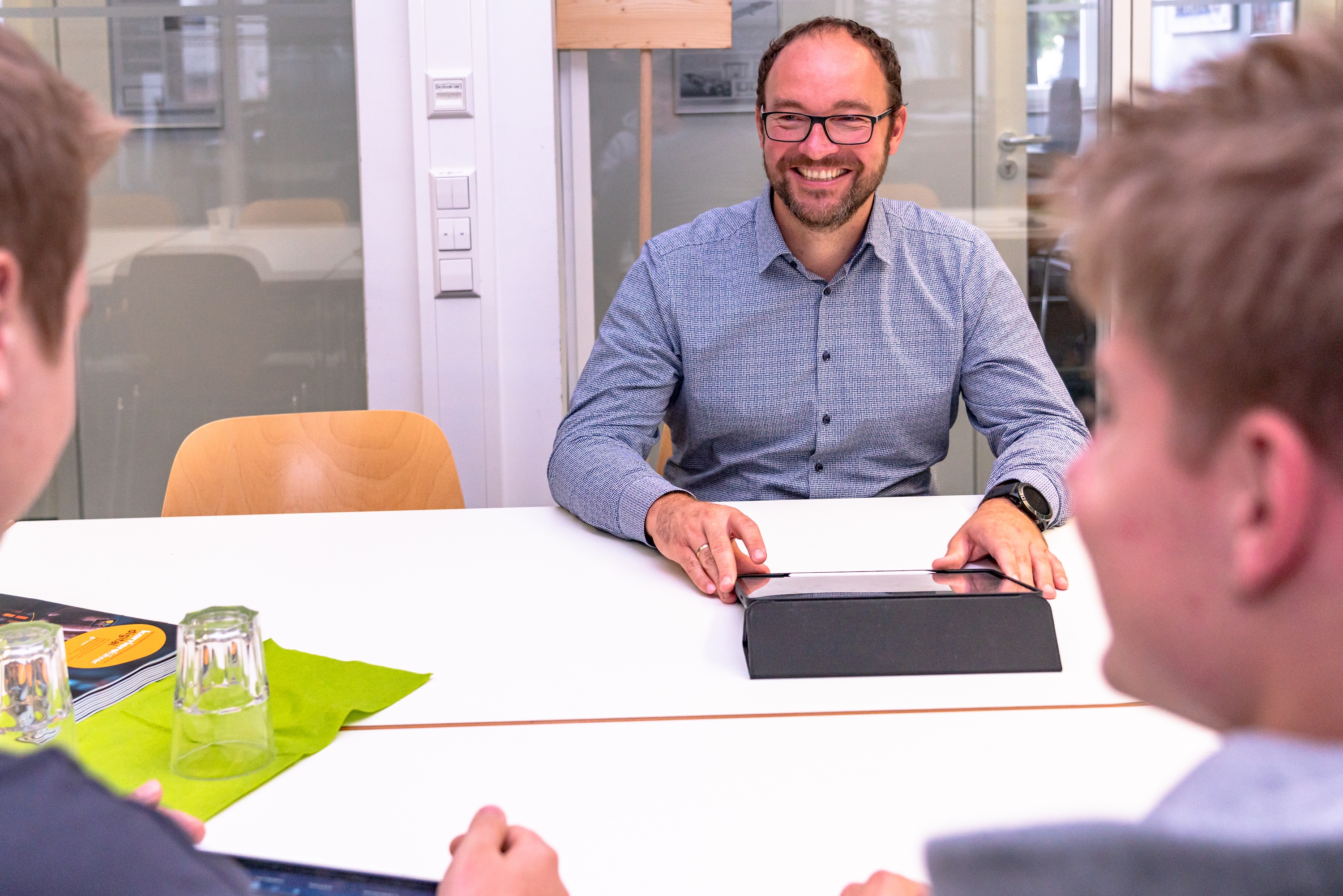 Mann sitzt mit zwei Studenten an einem Tisch