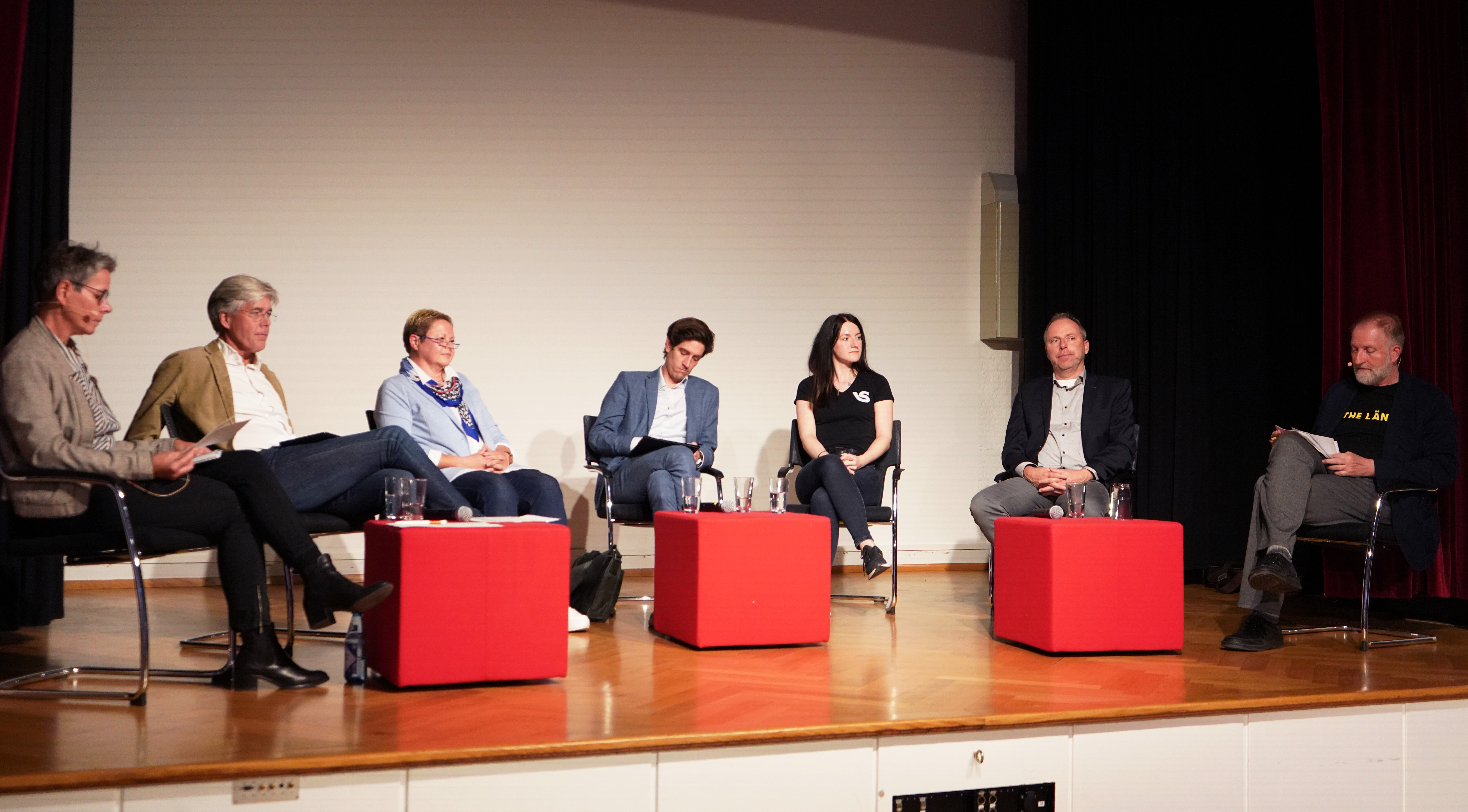 7 Personen auf Bühne bei Podiumsdiskussion
