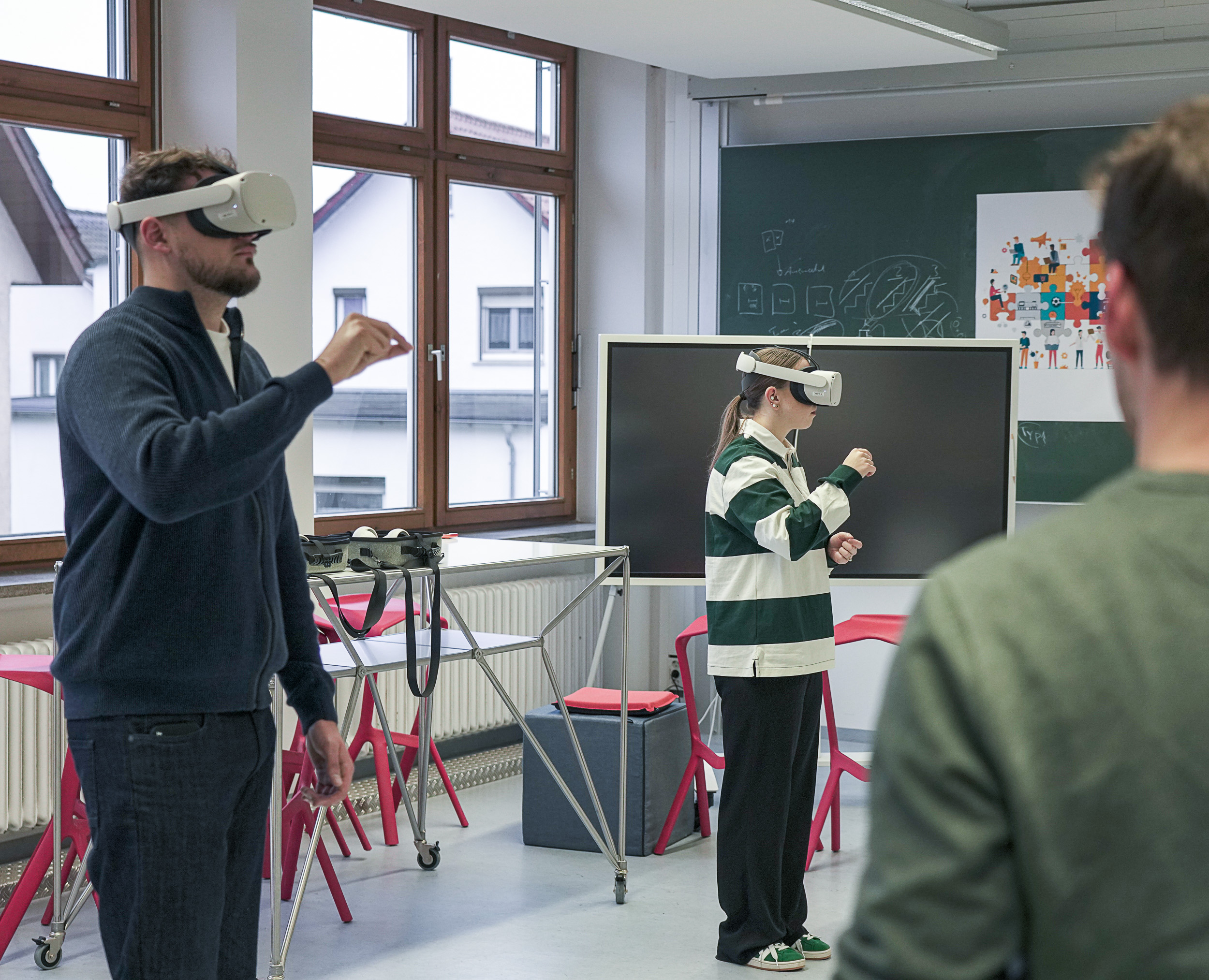 Drei Personen stehen in einem Raum. Zwei tragen eine VR-Brille