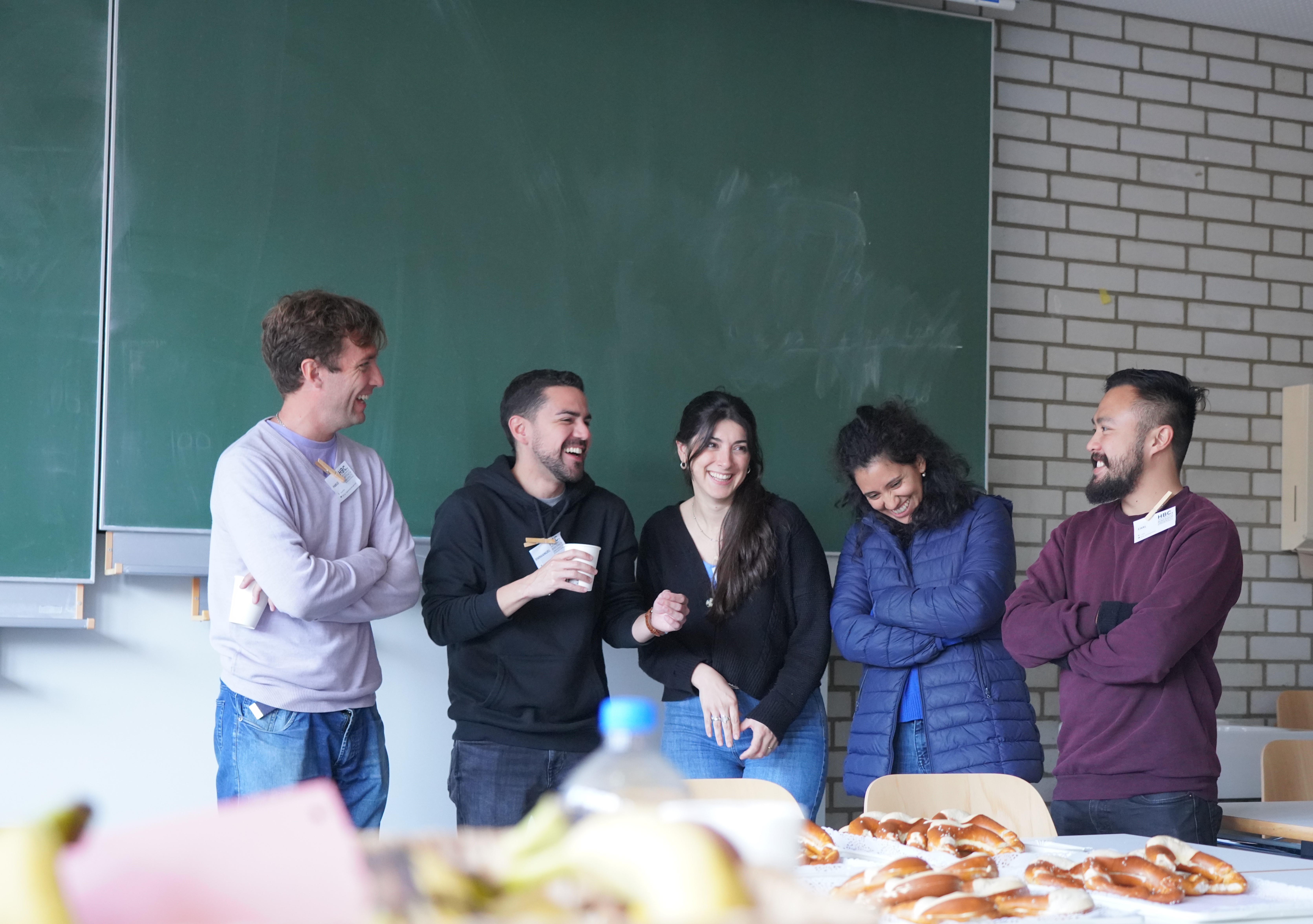 Fünf Personen verschiedener Nationen stehen lachend vor einem Buffet