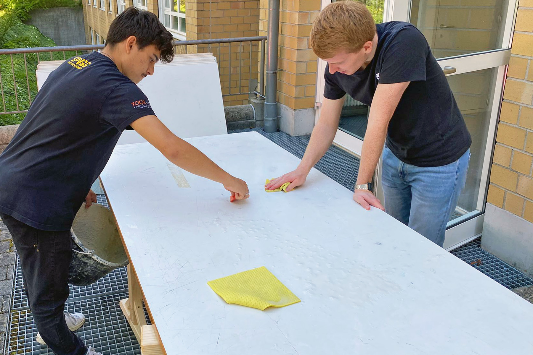 Zwei männliche Studierende bearbeiten Holzplatten die im späteren Materialverkauf zum Einsatz kommen