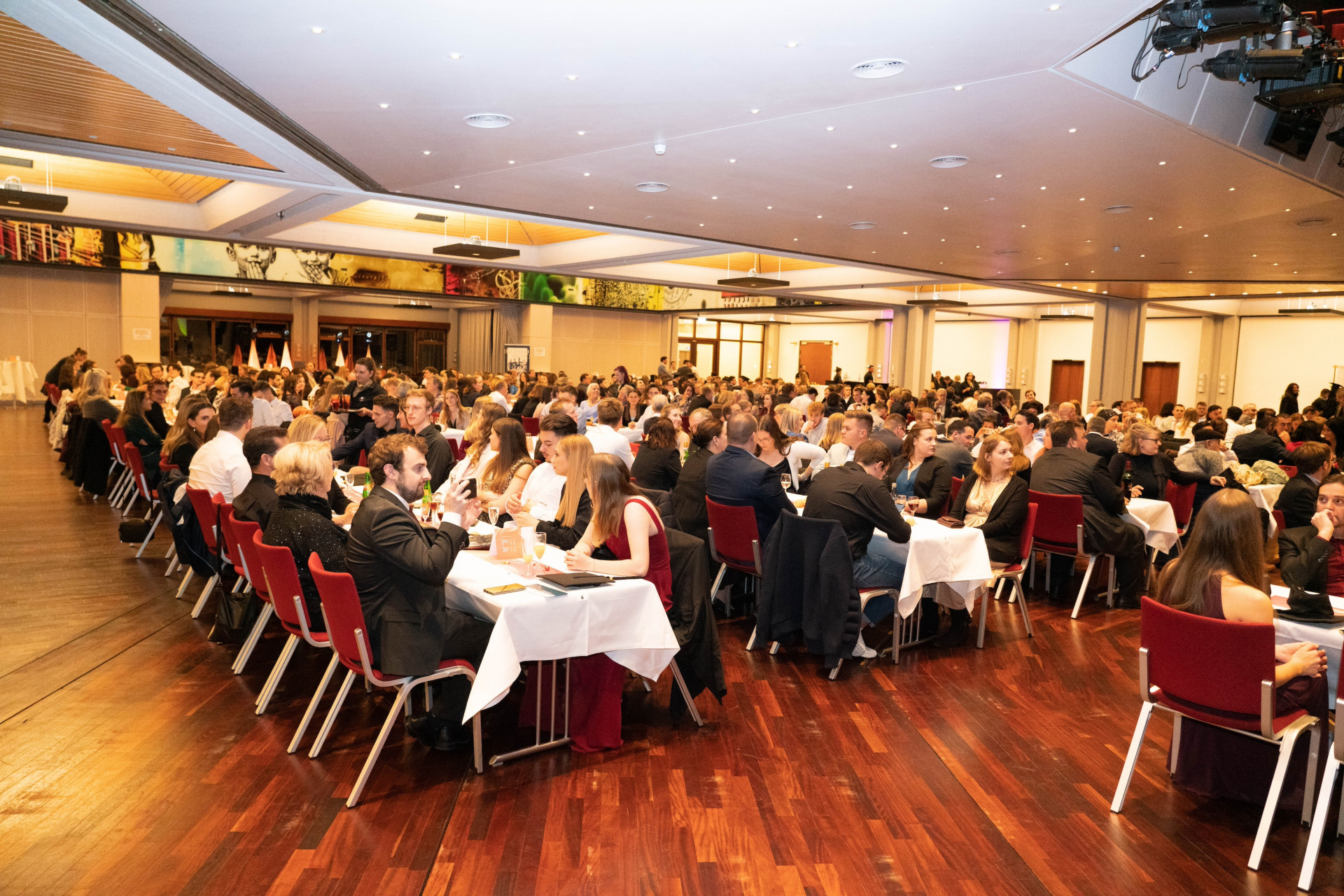 Menschen sitzen an Tischen in großem Saal