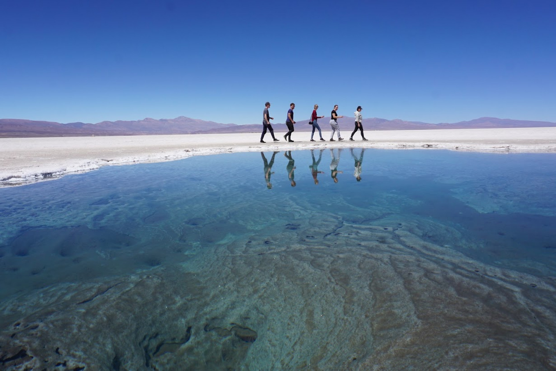 Menschen spiegeln sich im Wasser der Salines Grandes in Argentinien