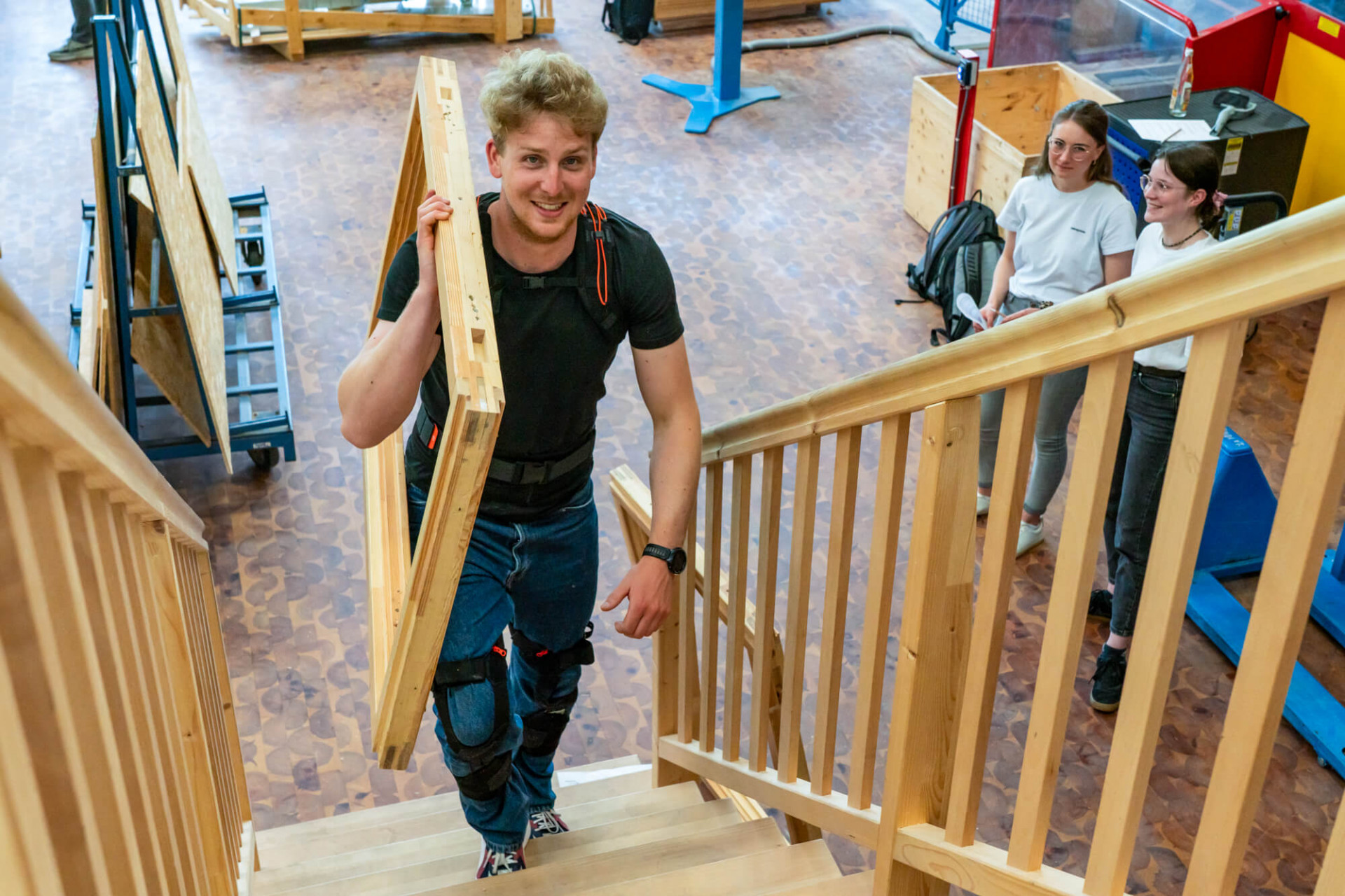 Ein Studierender geht mit schwerer Last und Exoskelett eine Treppe nach oben