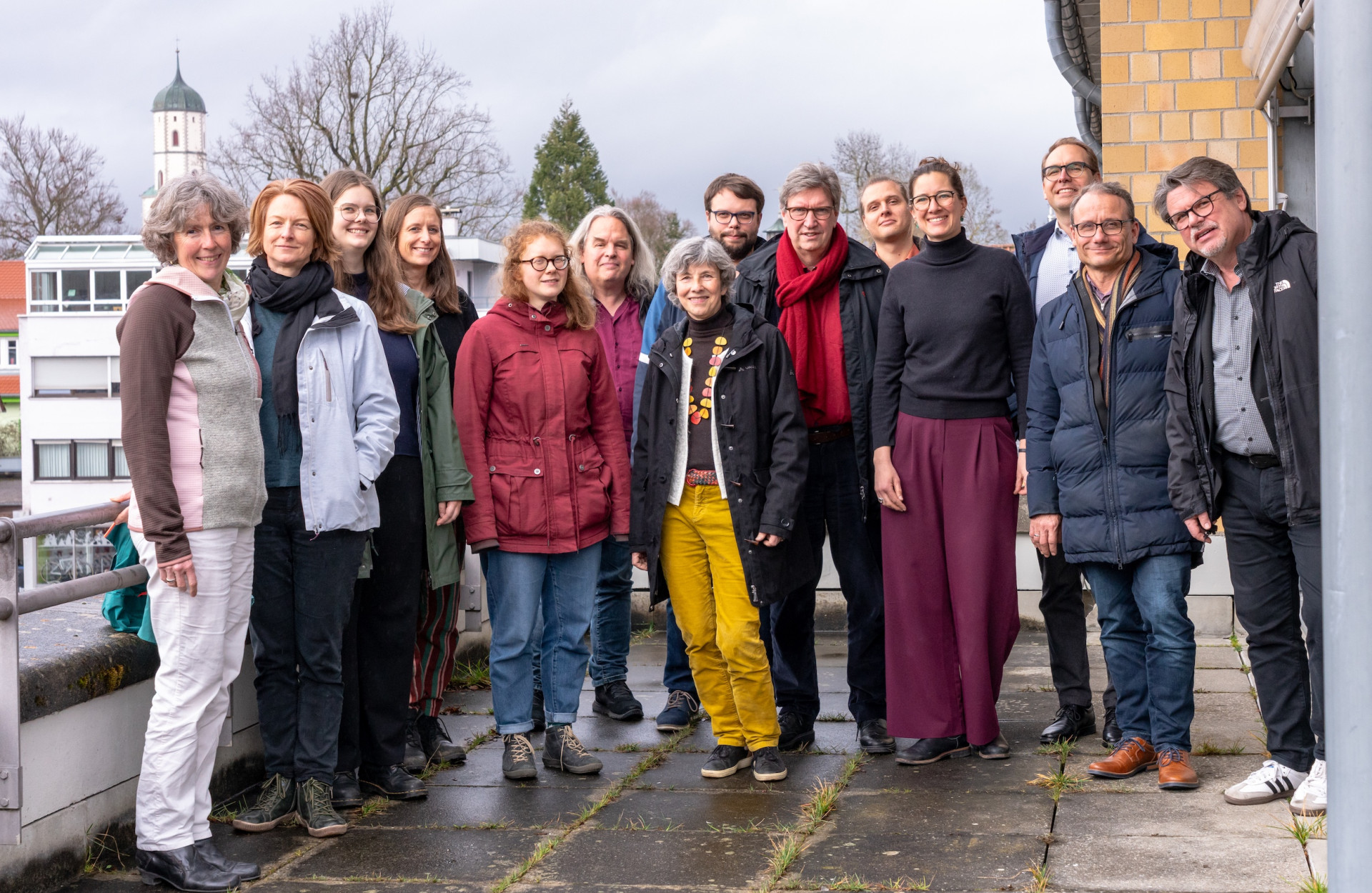 Viele Personen stehen draußen und lachen in die Kamera