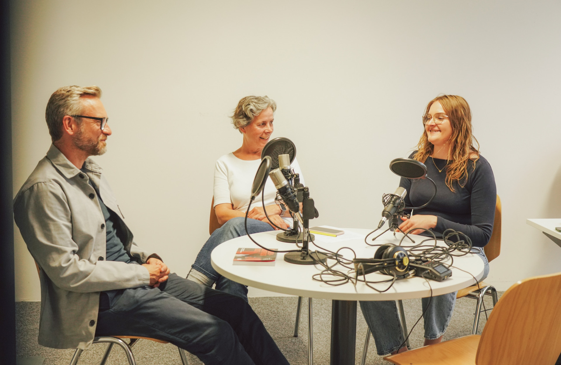 Drei Personen sitzen an einem runden Tisch bei einer Podcastaufnahme