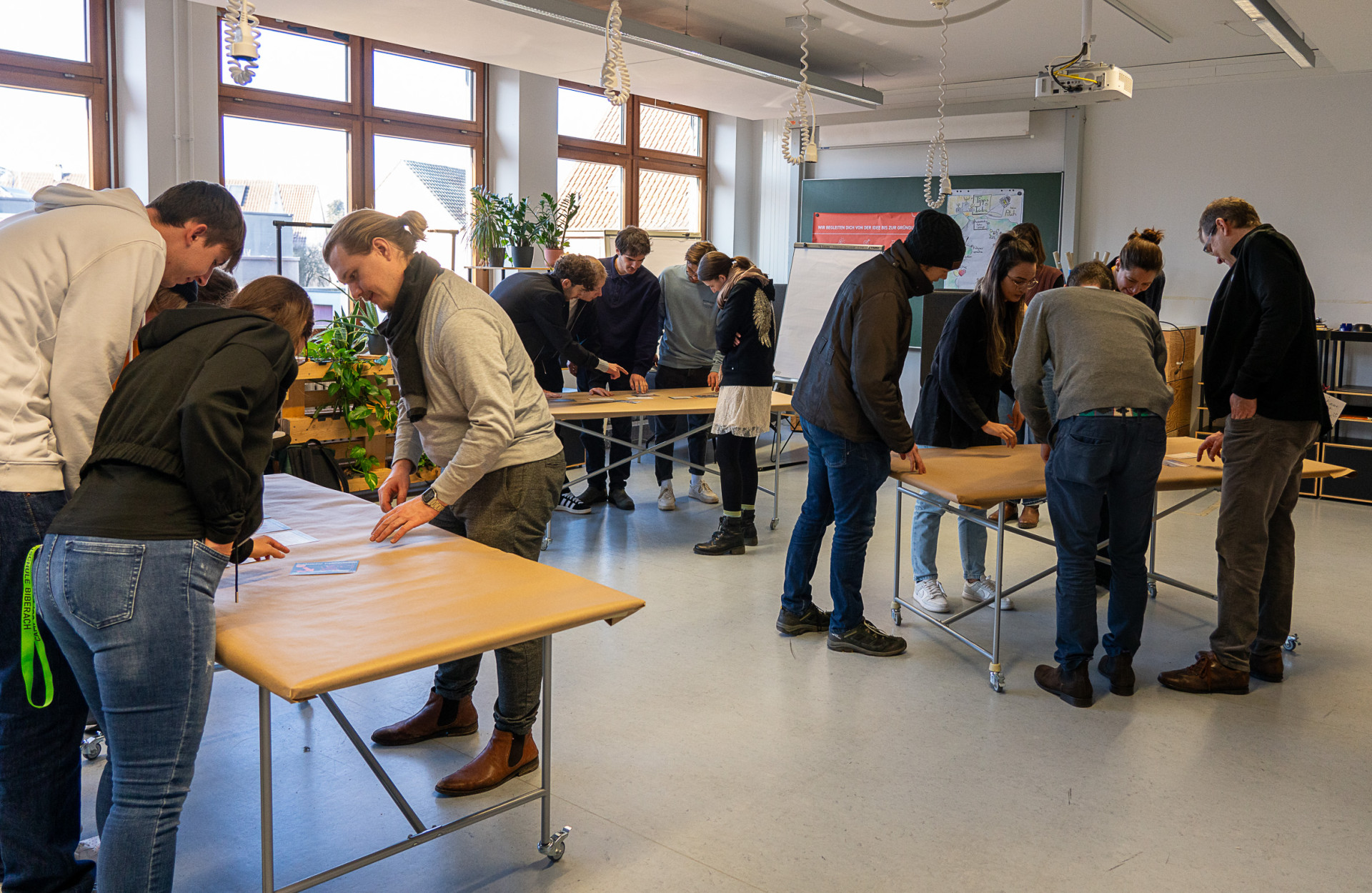 Personen stehen um drei Tische herum und arbeiten interaktiv