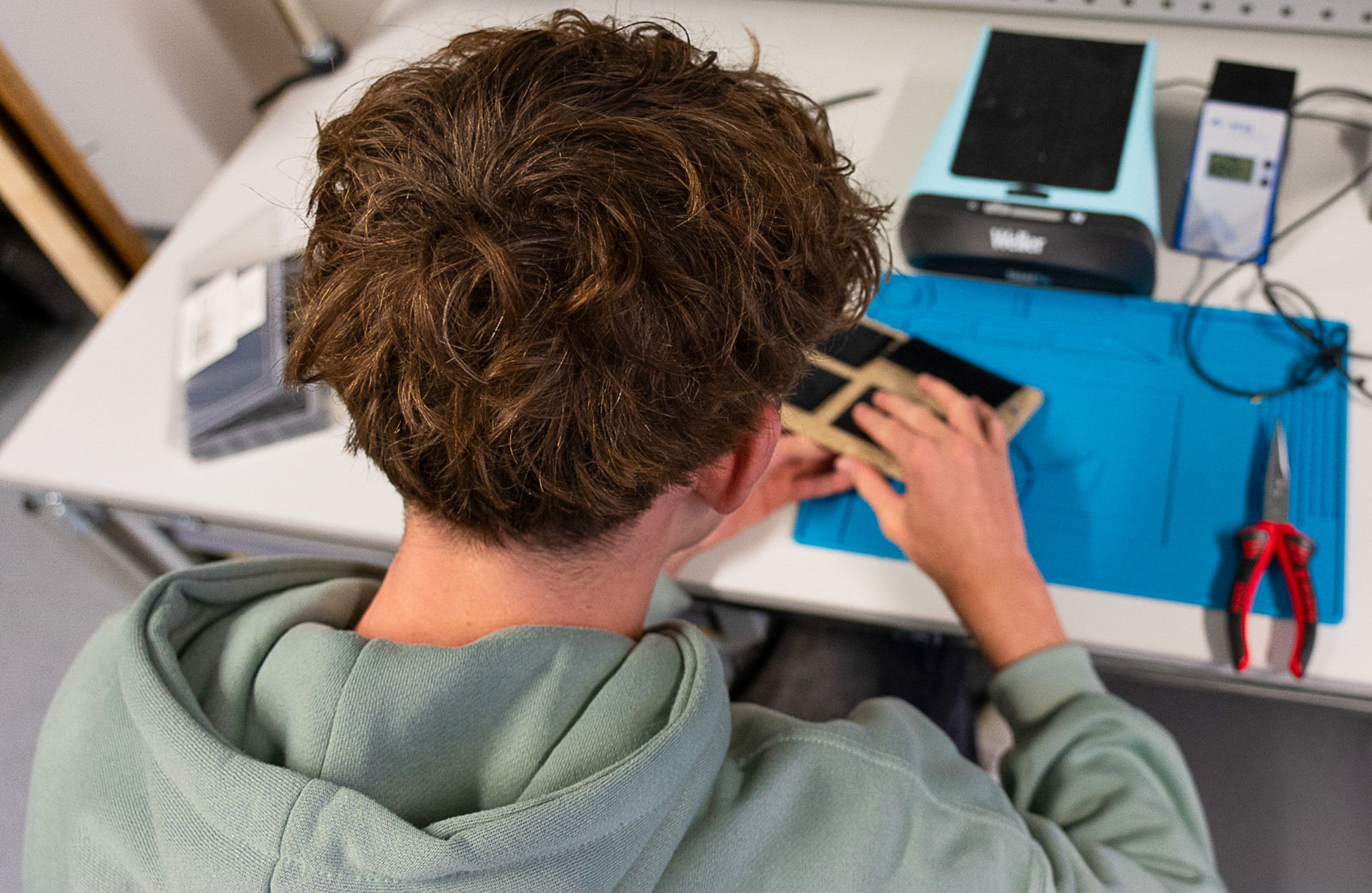 ein Junge sitzt an einem Schreibtisch und schraubt etwas zusammen