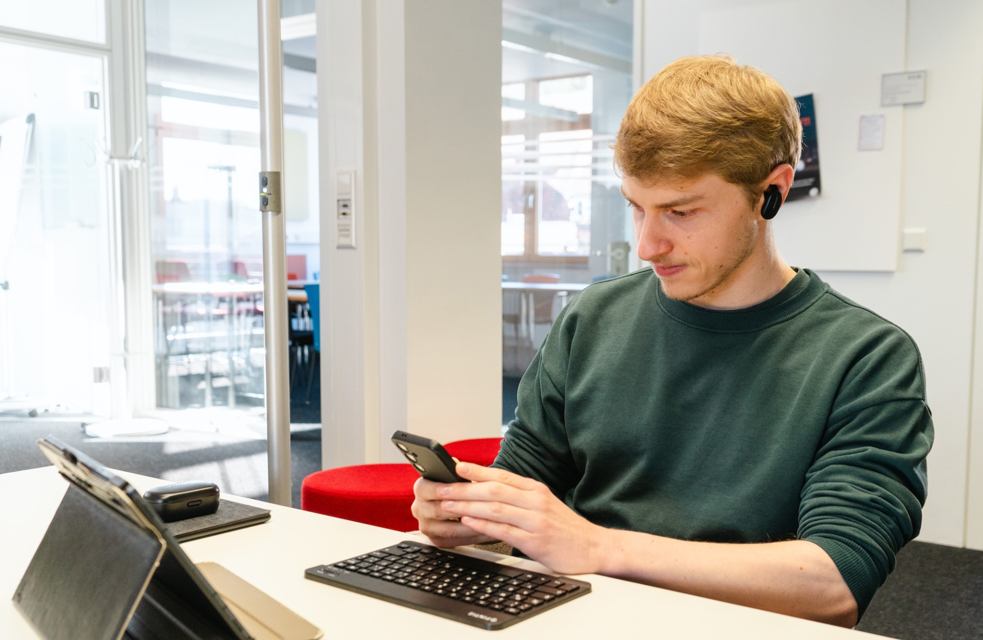 Ein junger Mann sitzt an einem Tisch und arbeitet am Laptop und Handy