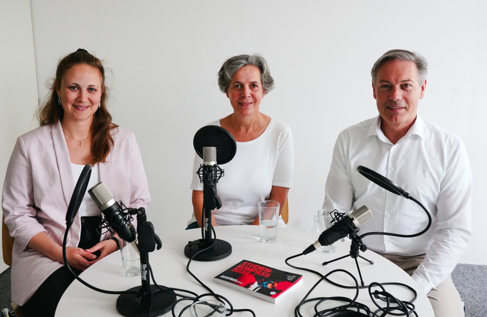Drei Personen sitzen bei einer Podcast-Aufnahme