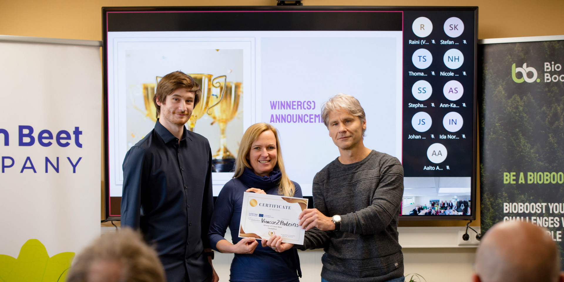 Ein Mann übergibt Urkunde an eine Frau und einen Mann