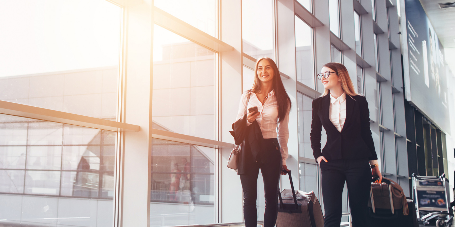 Zwei Frauen ziehen einen Koffer, sie sind auf einer Businessreise 