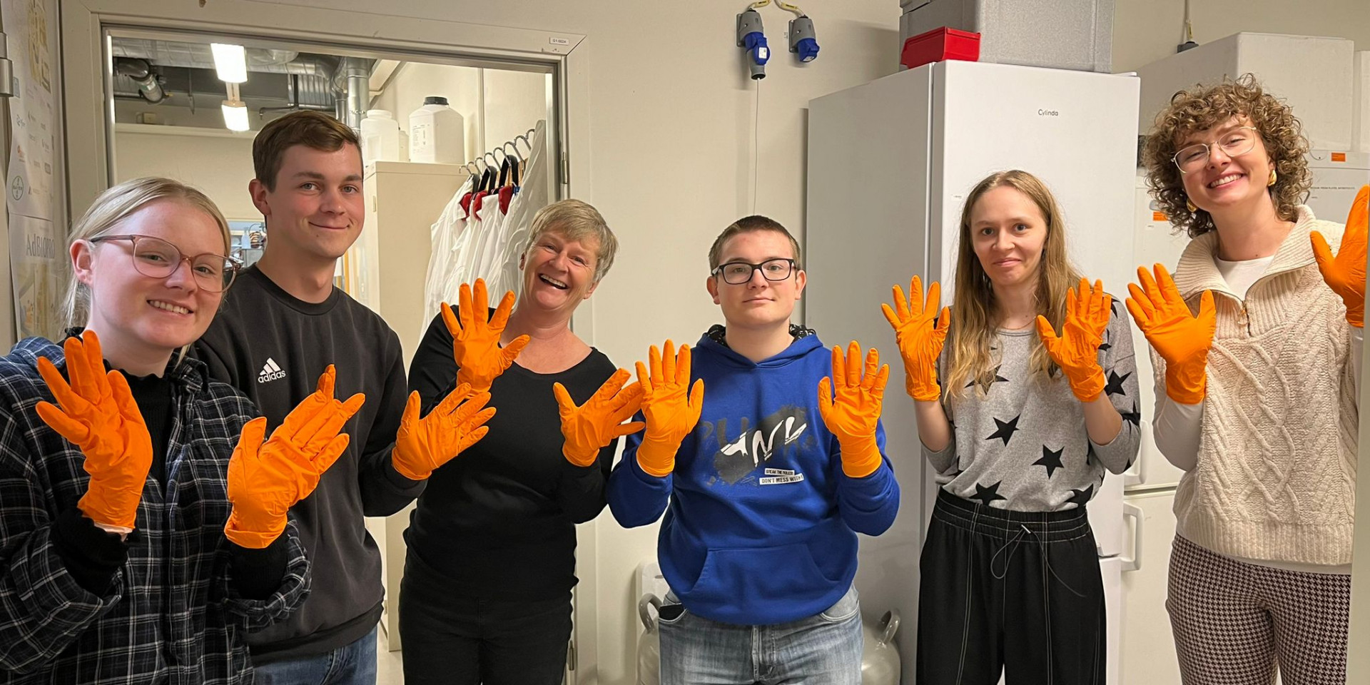 Sechs Personen mit orangen Handschuhen lächeln in die Kamera