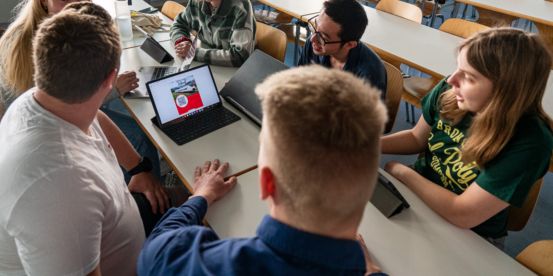 Sechs Studierende sitzen um einen Tisch mit geöffnetem Laptop
