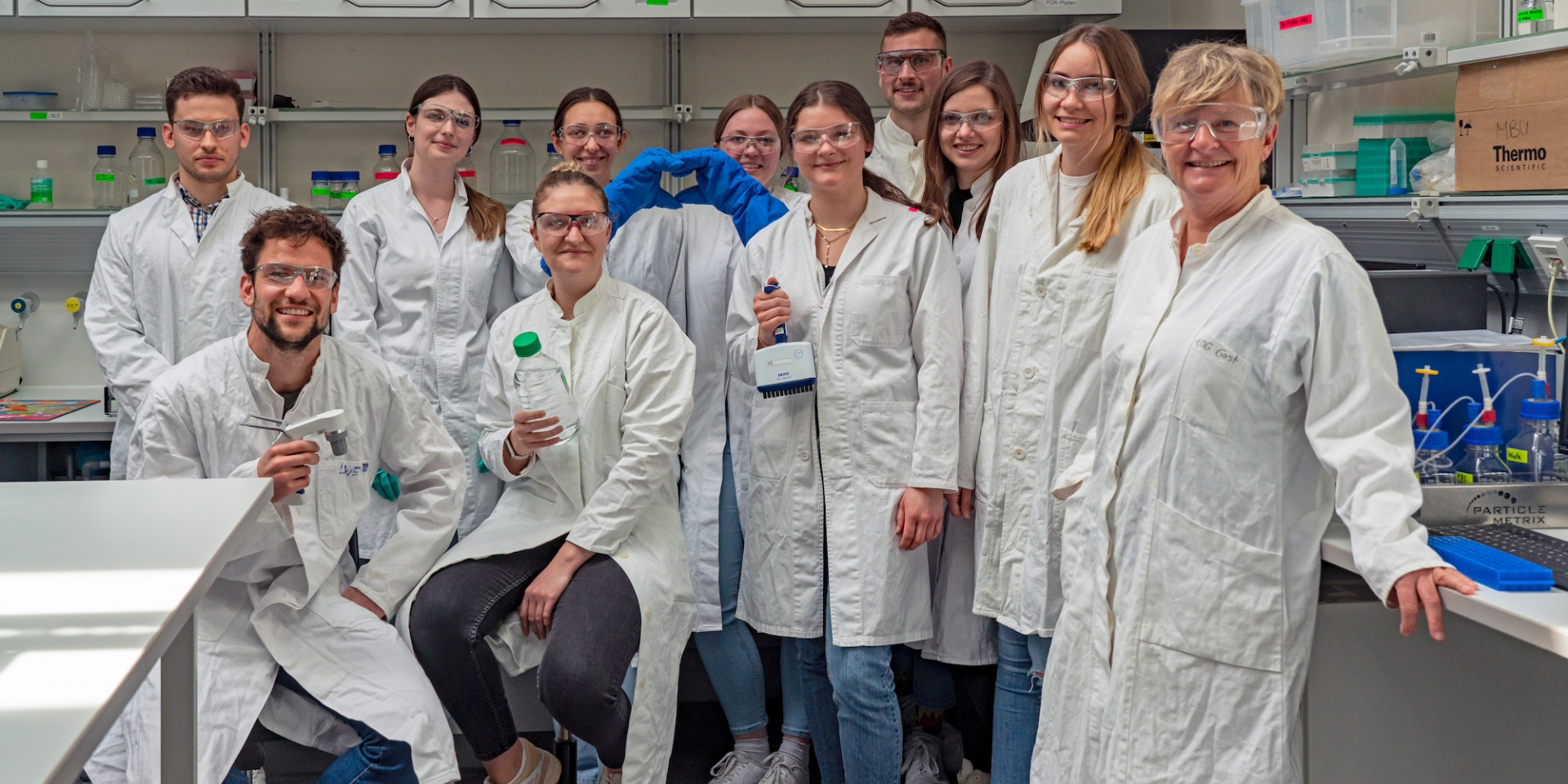 Gruppe von Menschen in Laborkitteln und mit Schutzbrillen