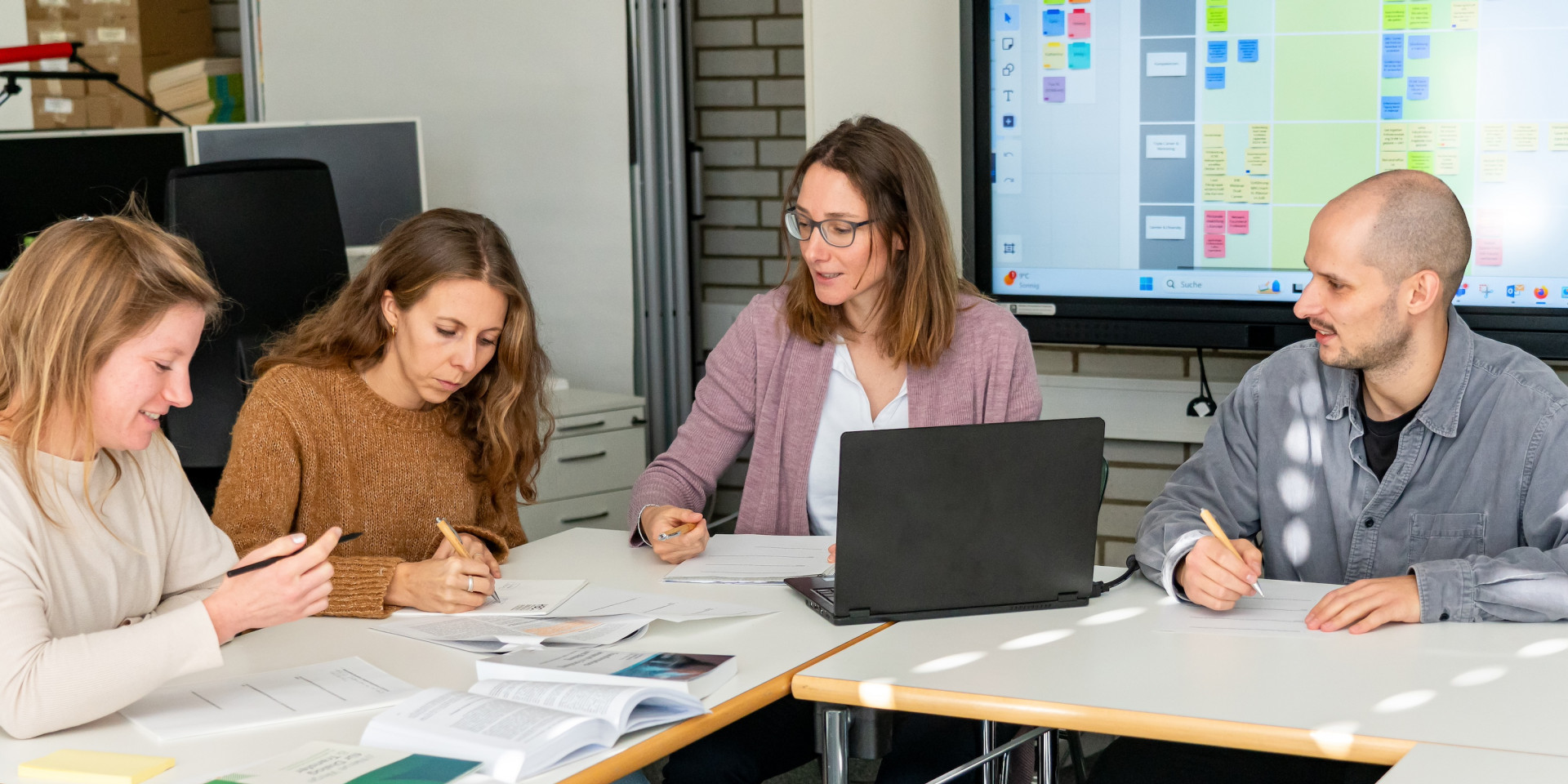 Drei Frauen und ein Mann sitzen an Tischen und arbeiten