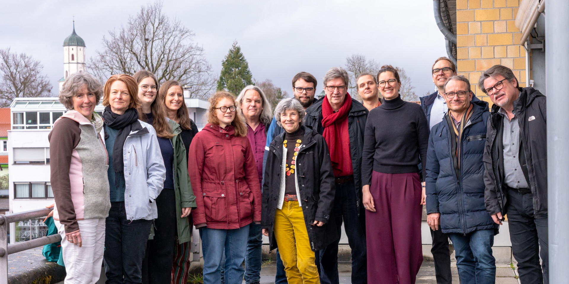 Viele Personen stehen draußen und lachen in die Kamera