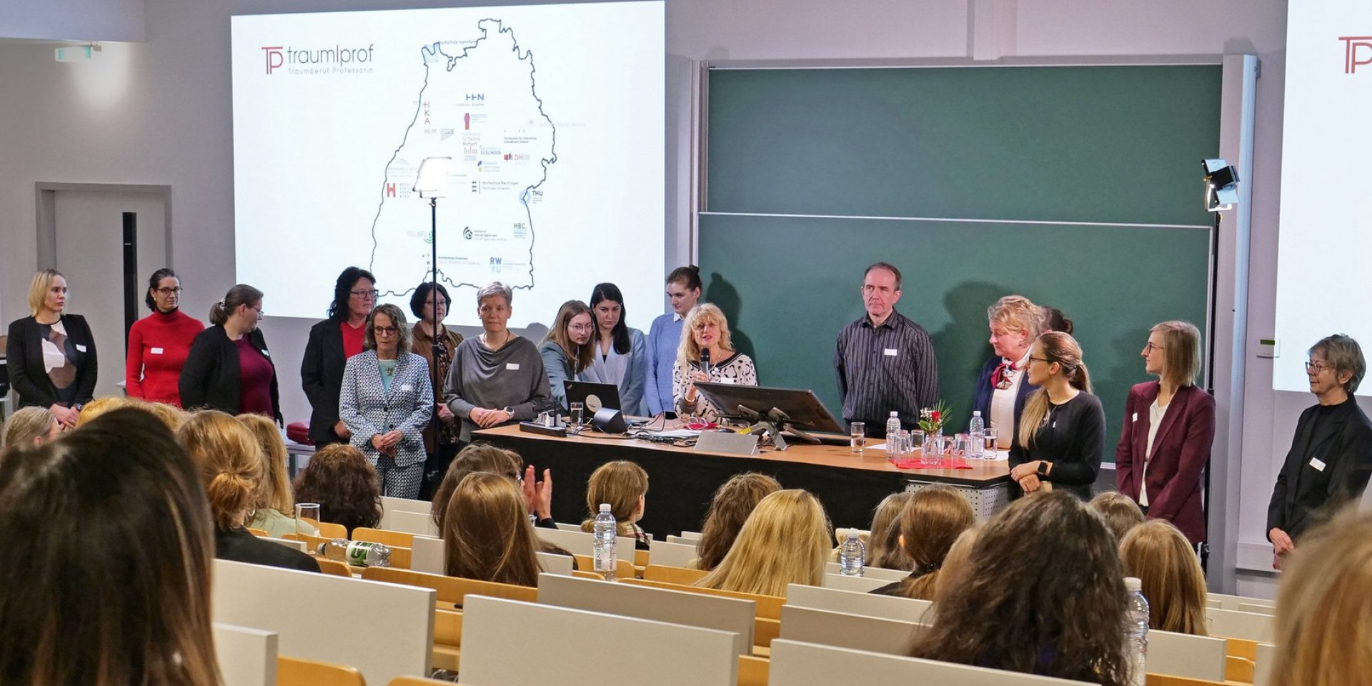 Viele Menschen stehen in Hörsaal vor Tafel