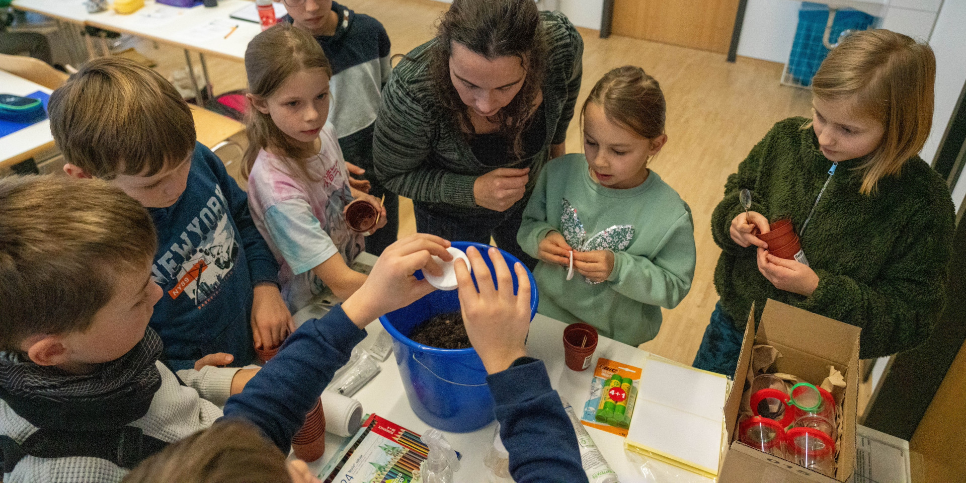 Kinder stehen mit Dozentin um Tisch und erforschen Boden