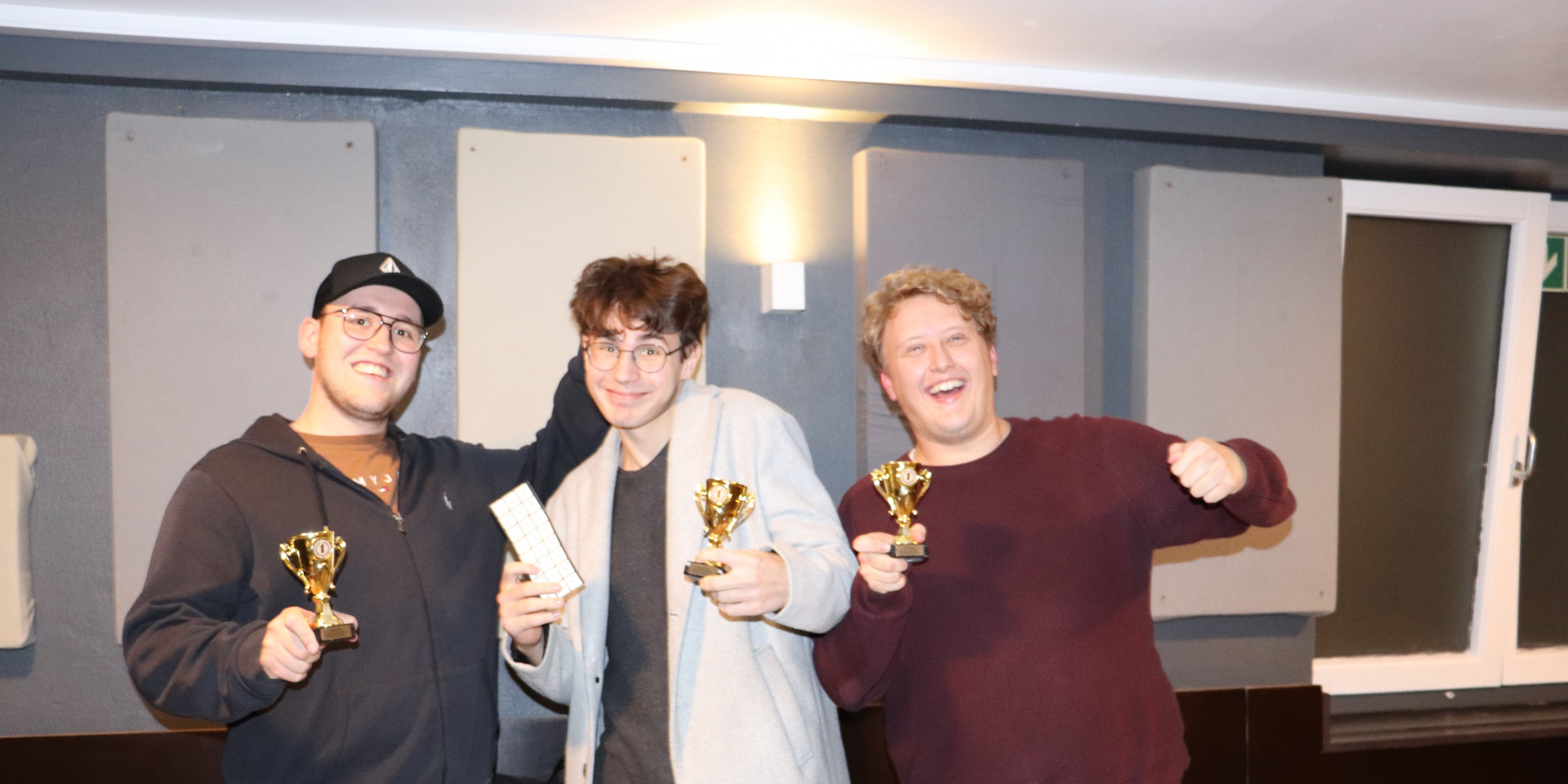 Drei Studenten mit Pokalen in der Hand, freuen sich über den Gewinn bei der KI Werkstatt Night