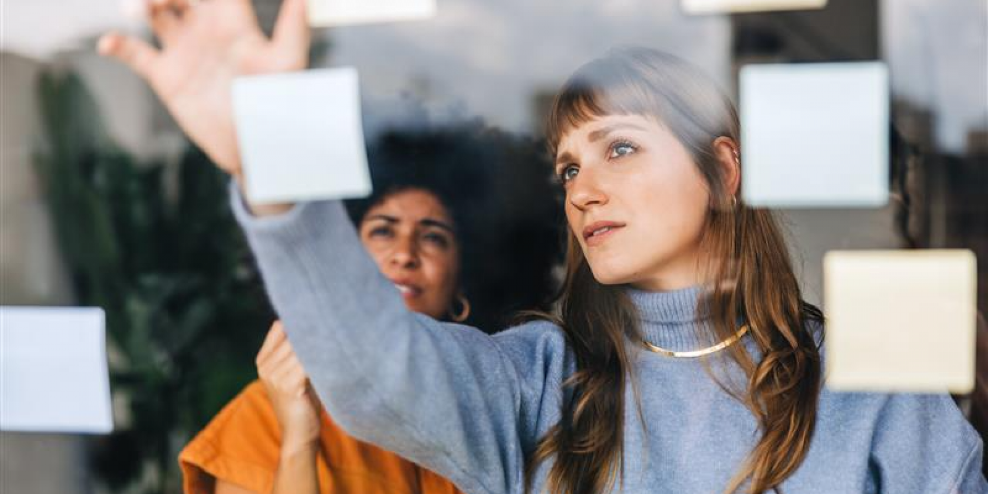 Zwei Frauen kleben Post it´s an eine Glasscheibe