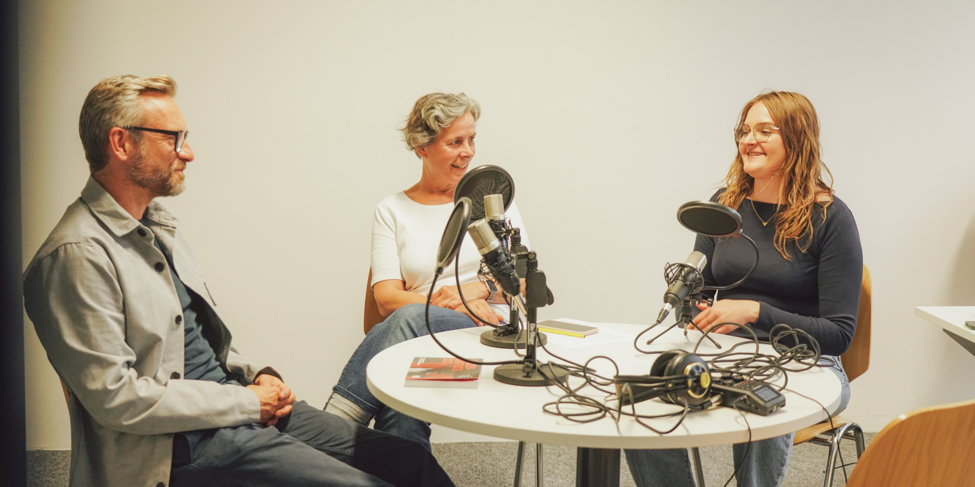 Drei Personen sitzen an einem runden Tisch bei einer Podcastaufnahme