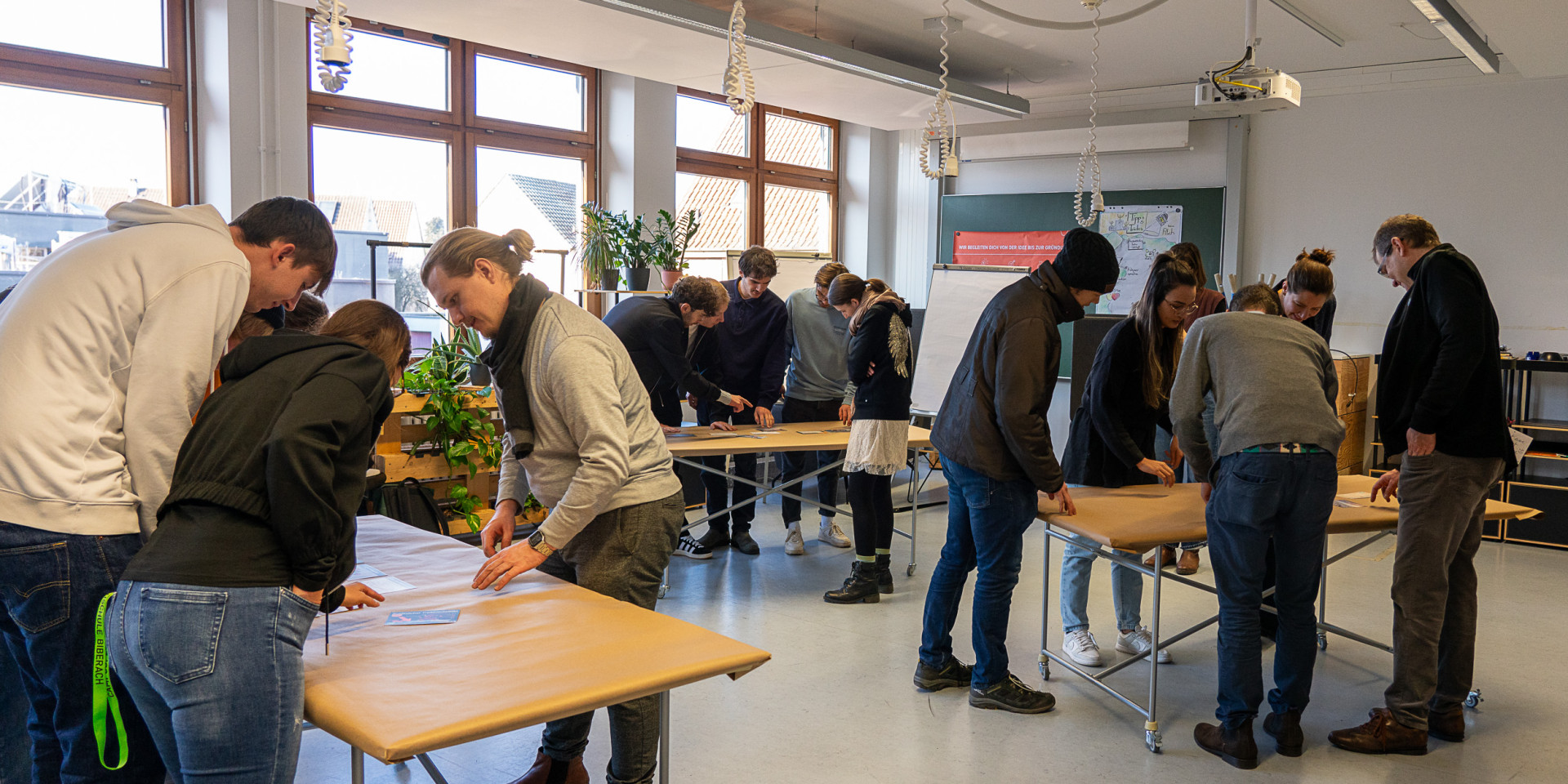 Personen stehen um drei Tische herum und arbeiten interaktiv