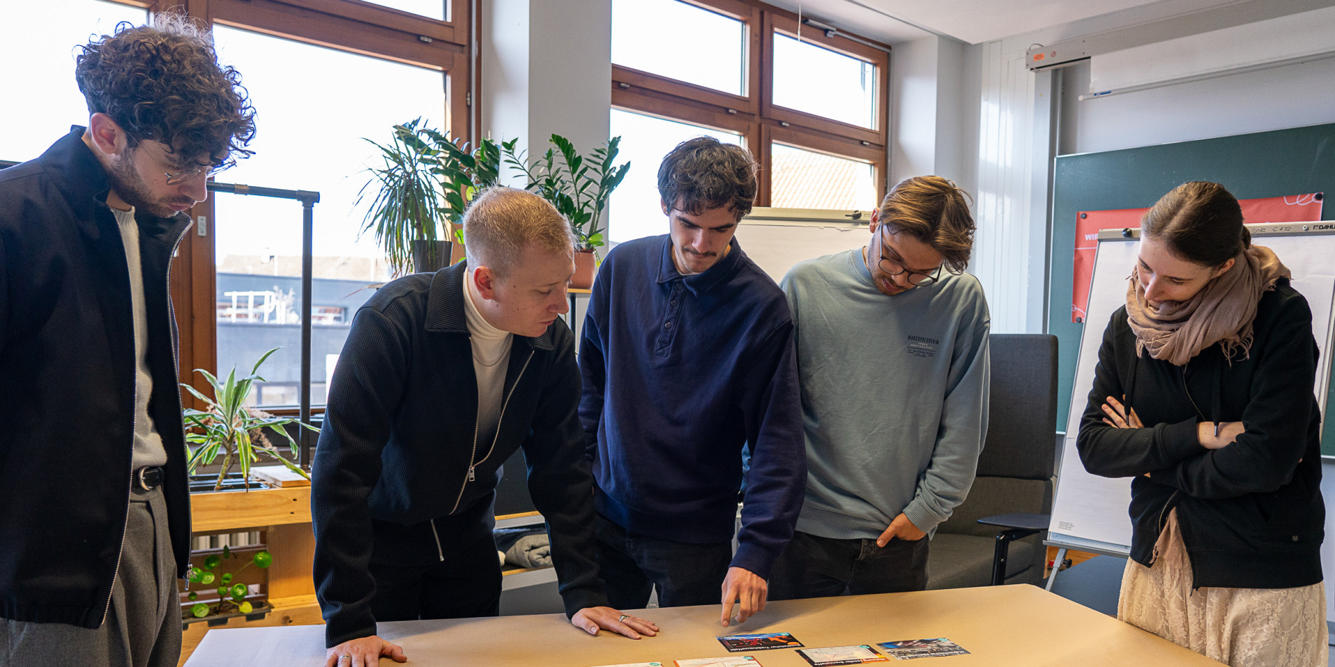 Personen stehen um einen Tisch herum und arbeiten interaktiv