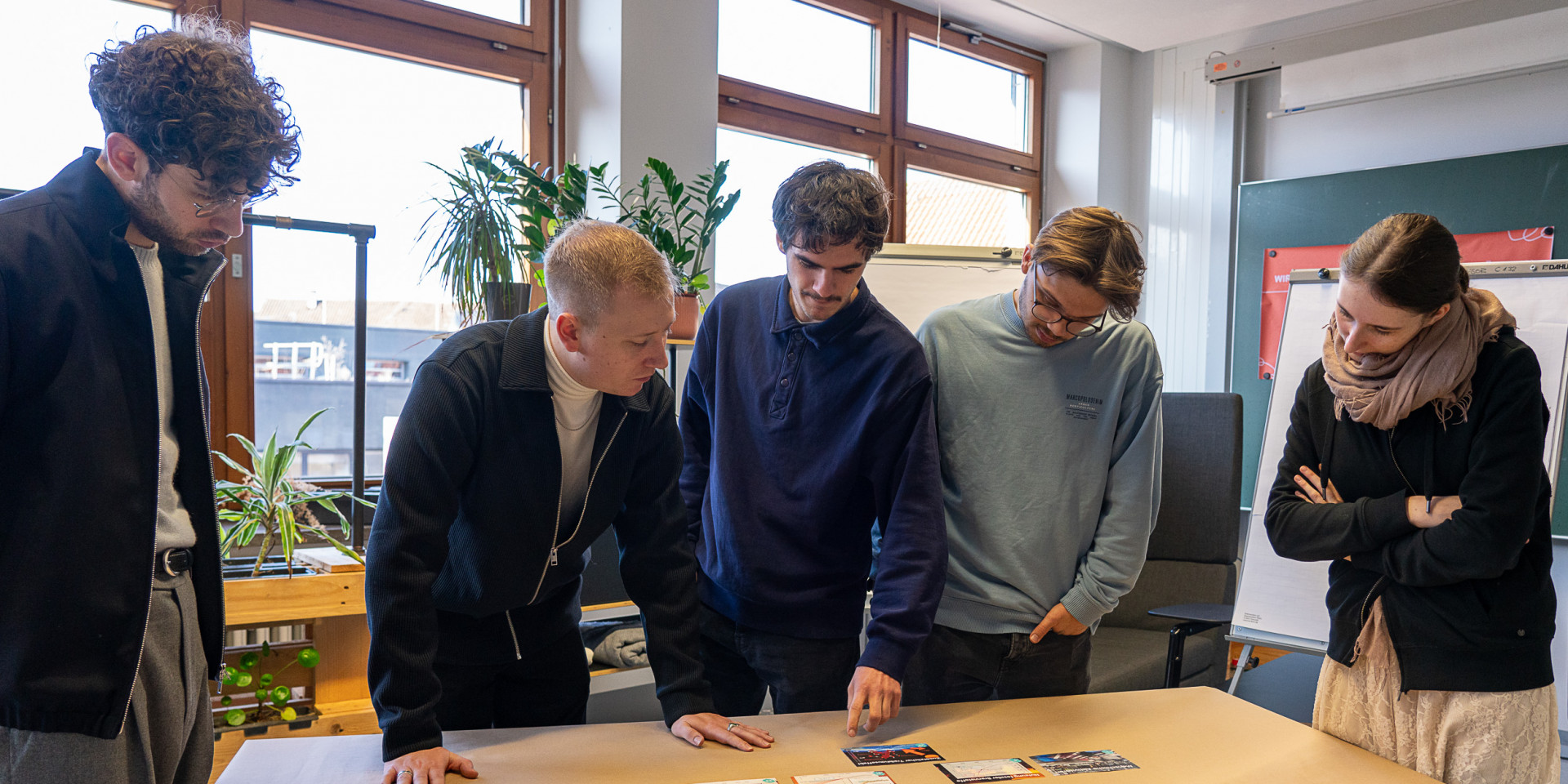 Personen stehen um einen Tisch herum und arbeiten interaktiv