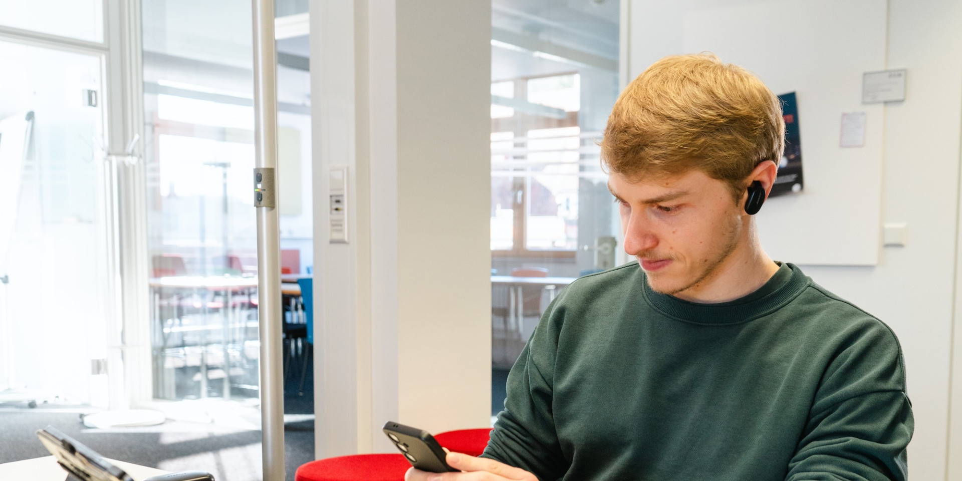 Ein junger Mann sitzt an einem Tisch und arbeitet am Laptop und Handy