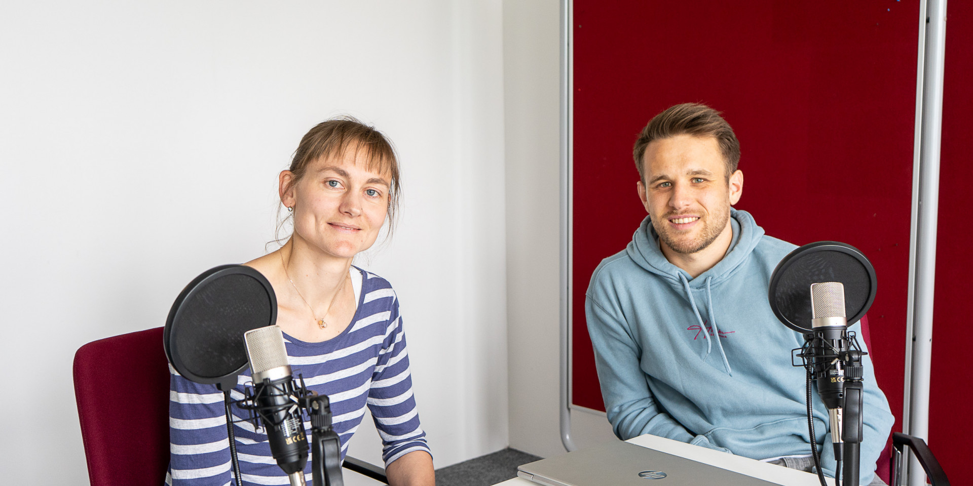 Eine Frau und ein Mann sitzen an einem Tisch und nehmen einen Podcast auf