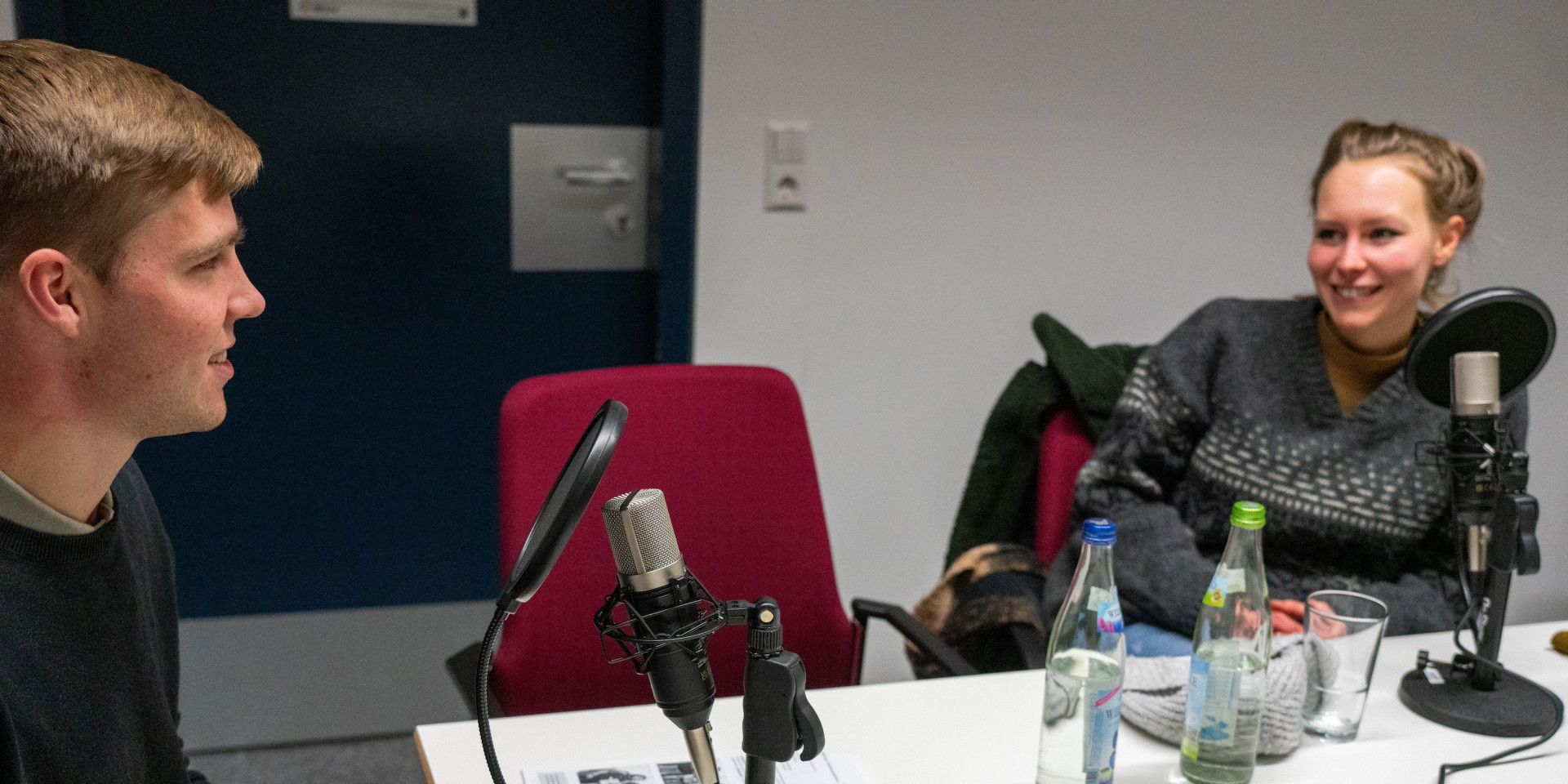 Ein Mann und eine Frau sitzen an einem Tisch bei Podcastaufnahme