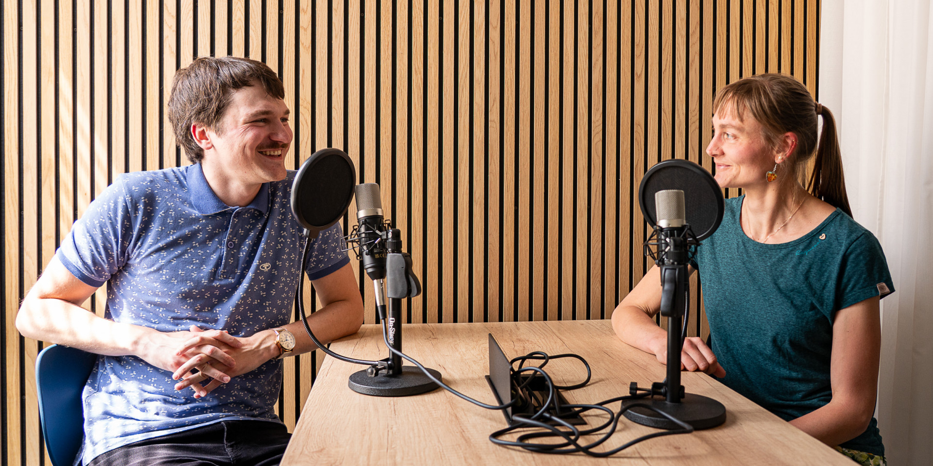 Eine Frau und ein Mann sitzen an einem Tisch und nehmen einen Podcast auf