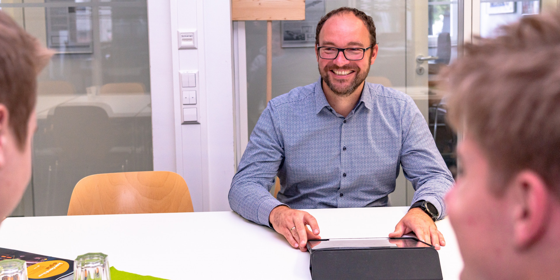 Mann sitzt mit zwei Studenten an einem Tisch