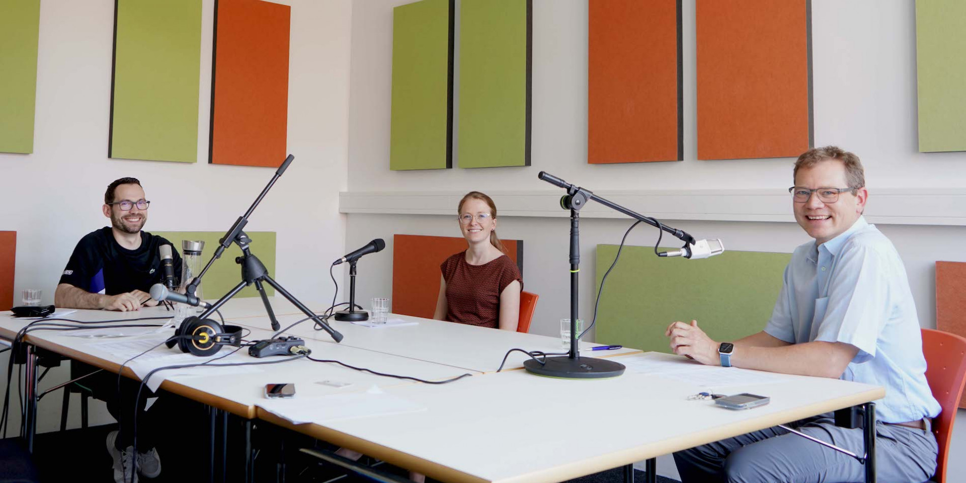 Drei Personen bei Podcastaufnahme an einem Tisch