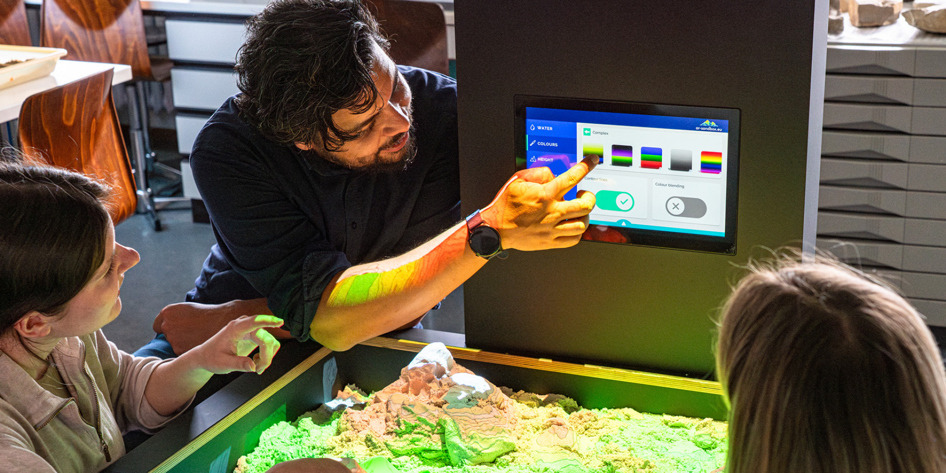 Professor Julius Jara gemeinsam mit zwei Studierenden an der AR-Sandbox