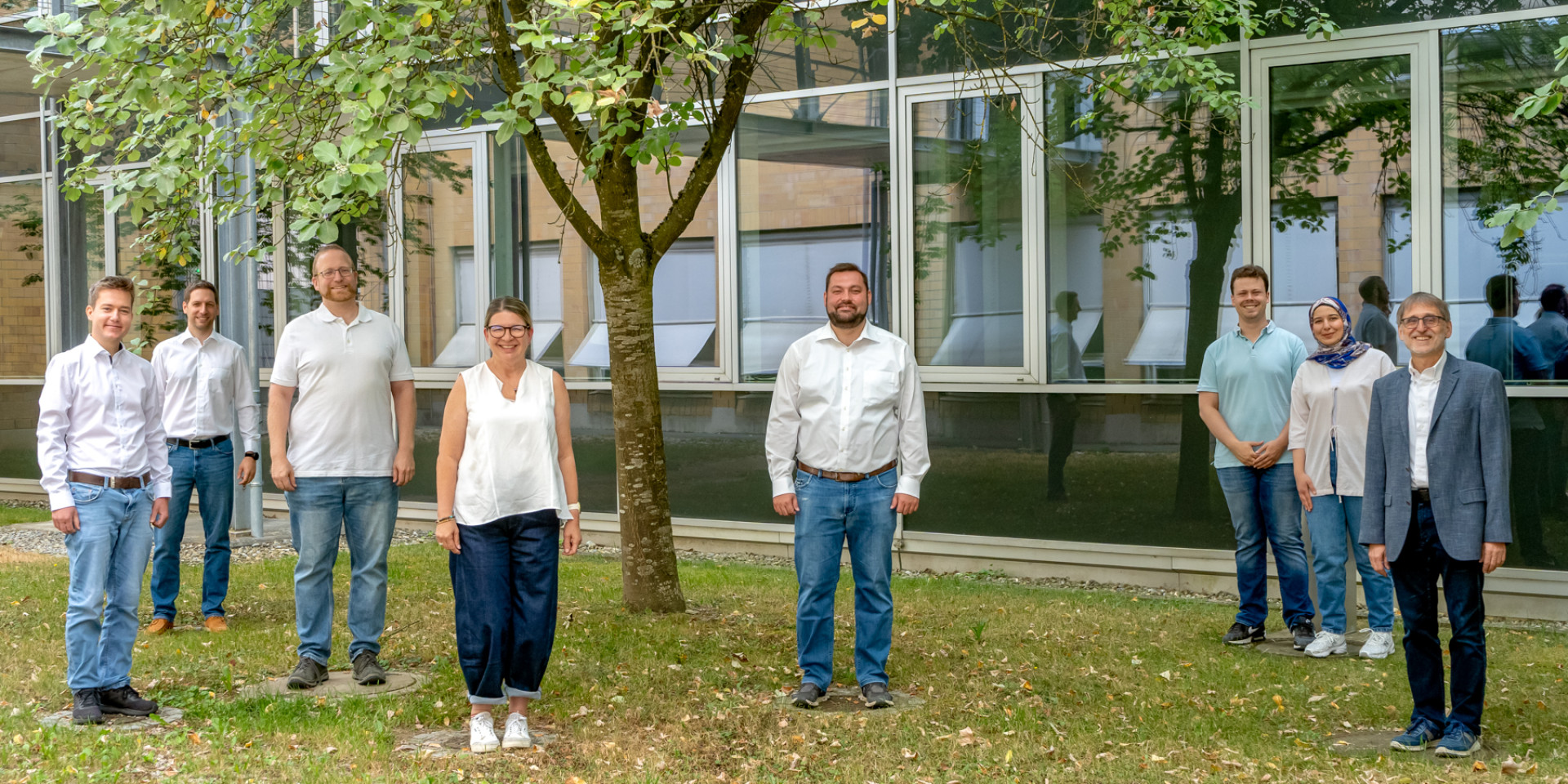 8 Mitarbeiter*innen stehen auf einer grünen Wiese