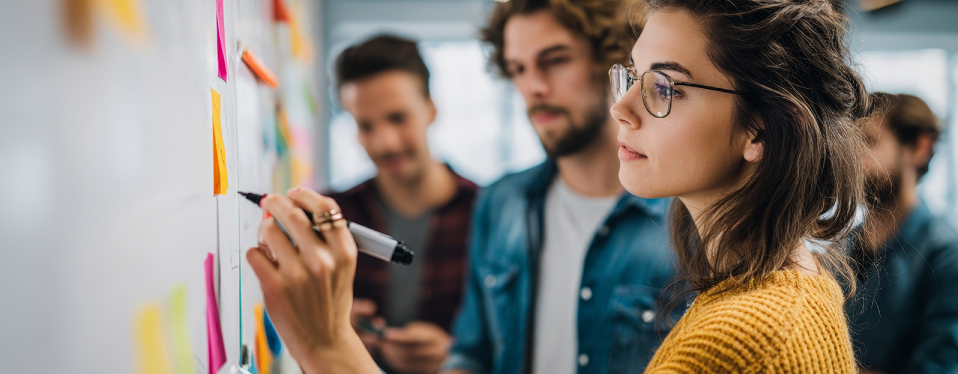 Studierende im legerem casual Look stehen mit Stift vor einem Whiteboard mit vielen bunten Post-its