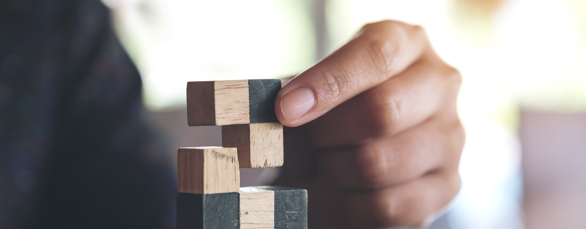 Eine Hand setzt Tetrisbausteine übereinander