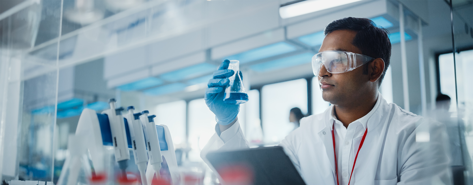 Männlicher Wissenschaftlers analysiert flüssige Biochemikalien in einem Erlenmeyerkolben und verwendet ein digitales Tablet in einem modernen Biotechnologielabor.