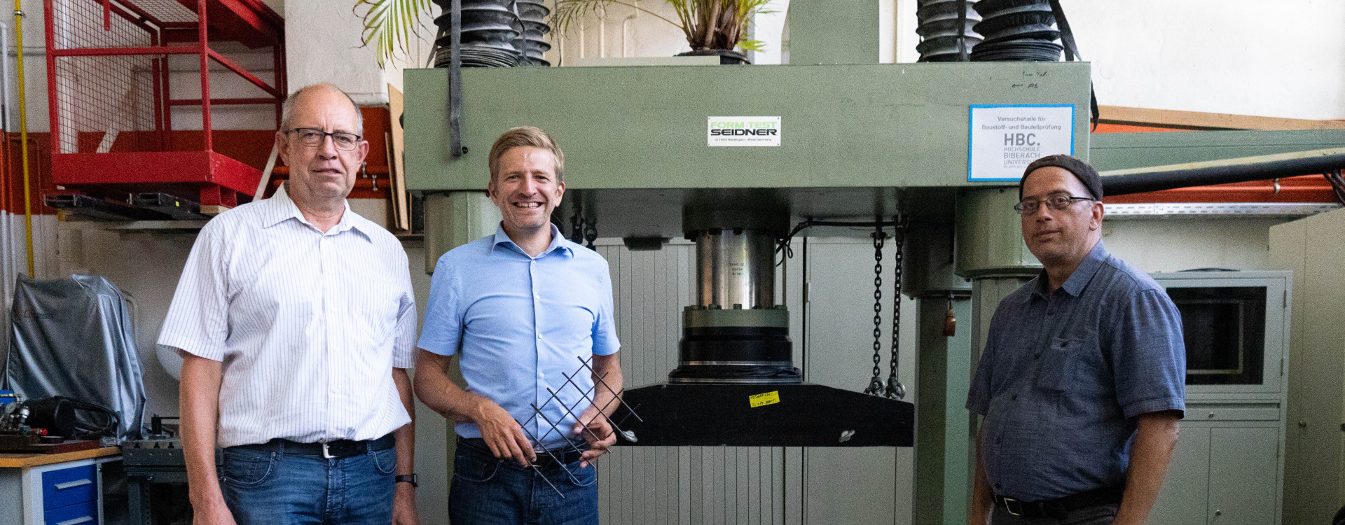 Drei Personen vor Prüfmaschine